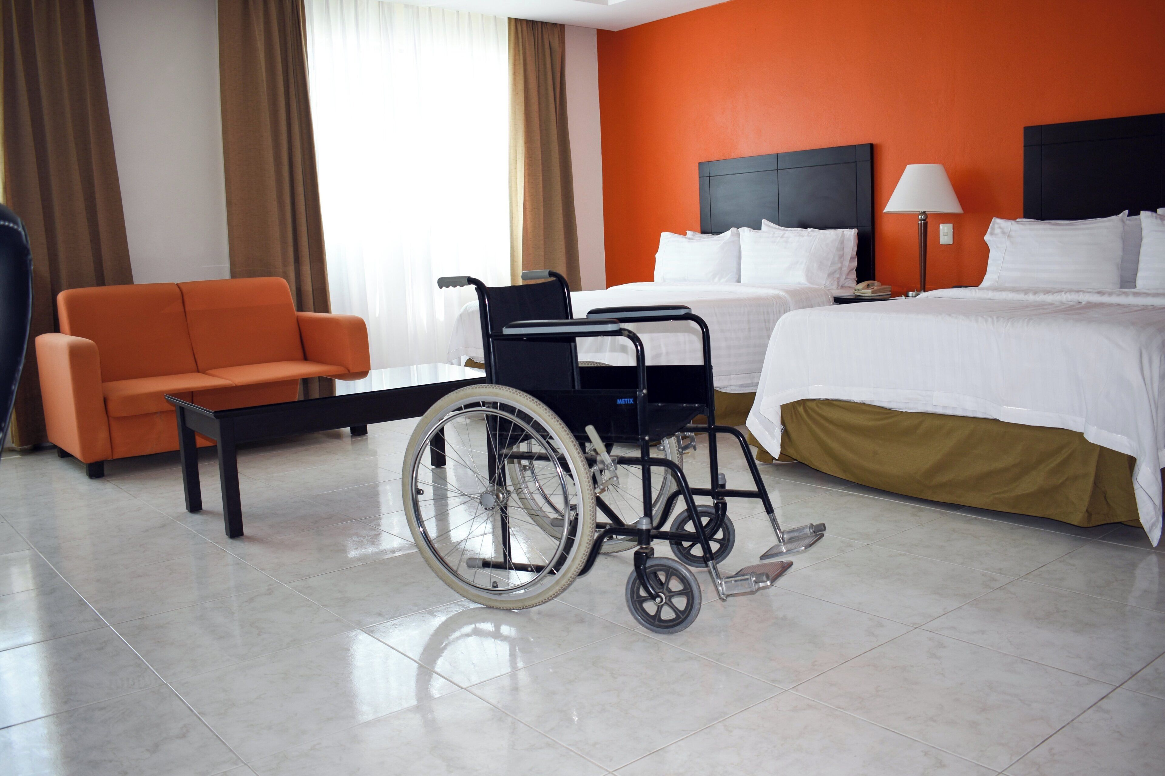 Habitación de hotel con silla de ruedas, cama, sofá y escritorio.