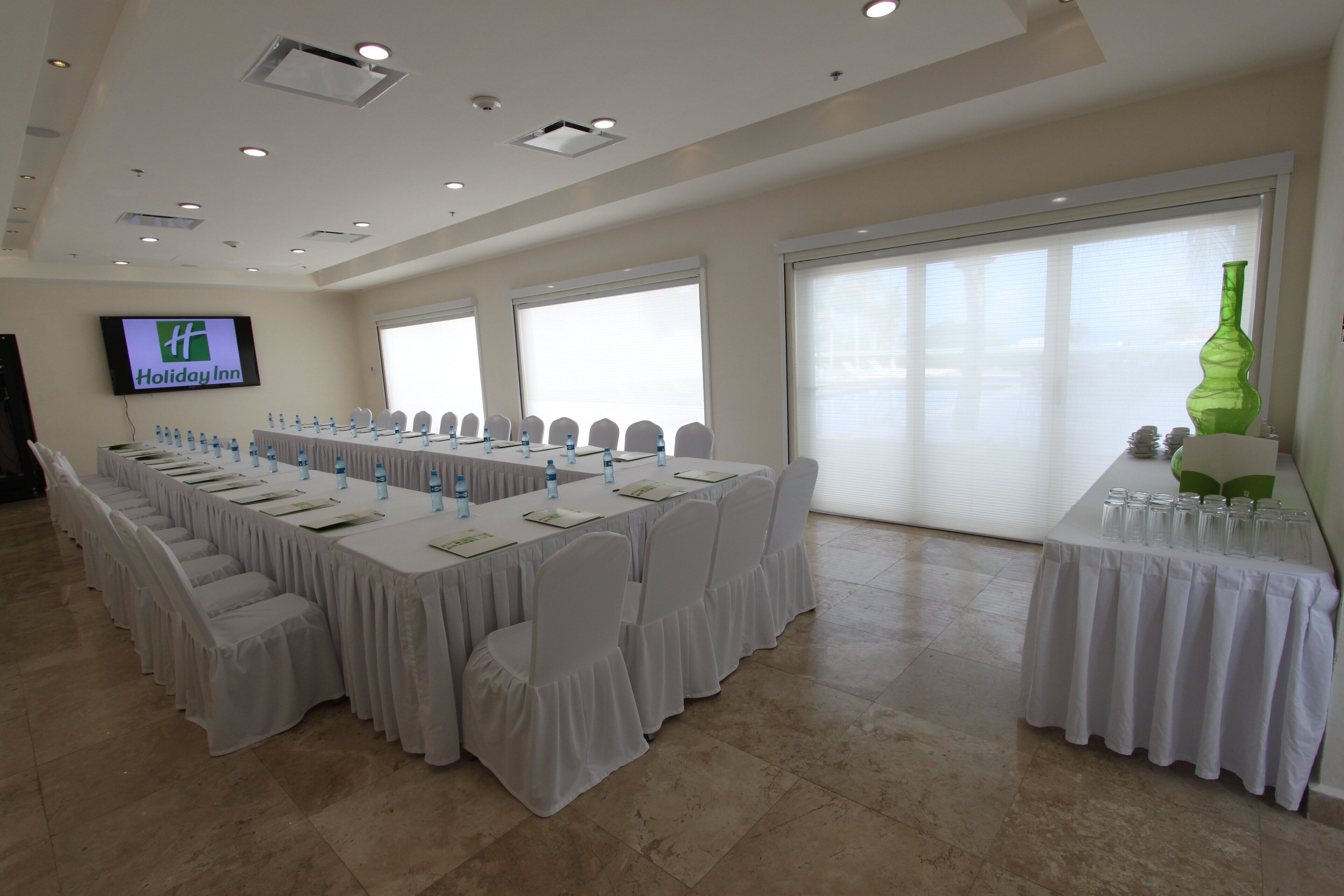 A conference room with a long table, chairs, and a television screen displaying 'Holiday Inn'.
