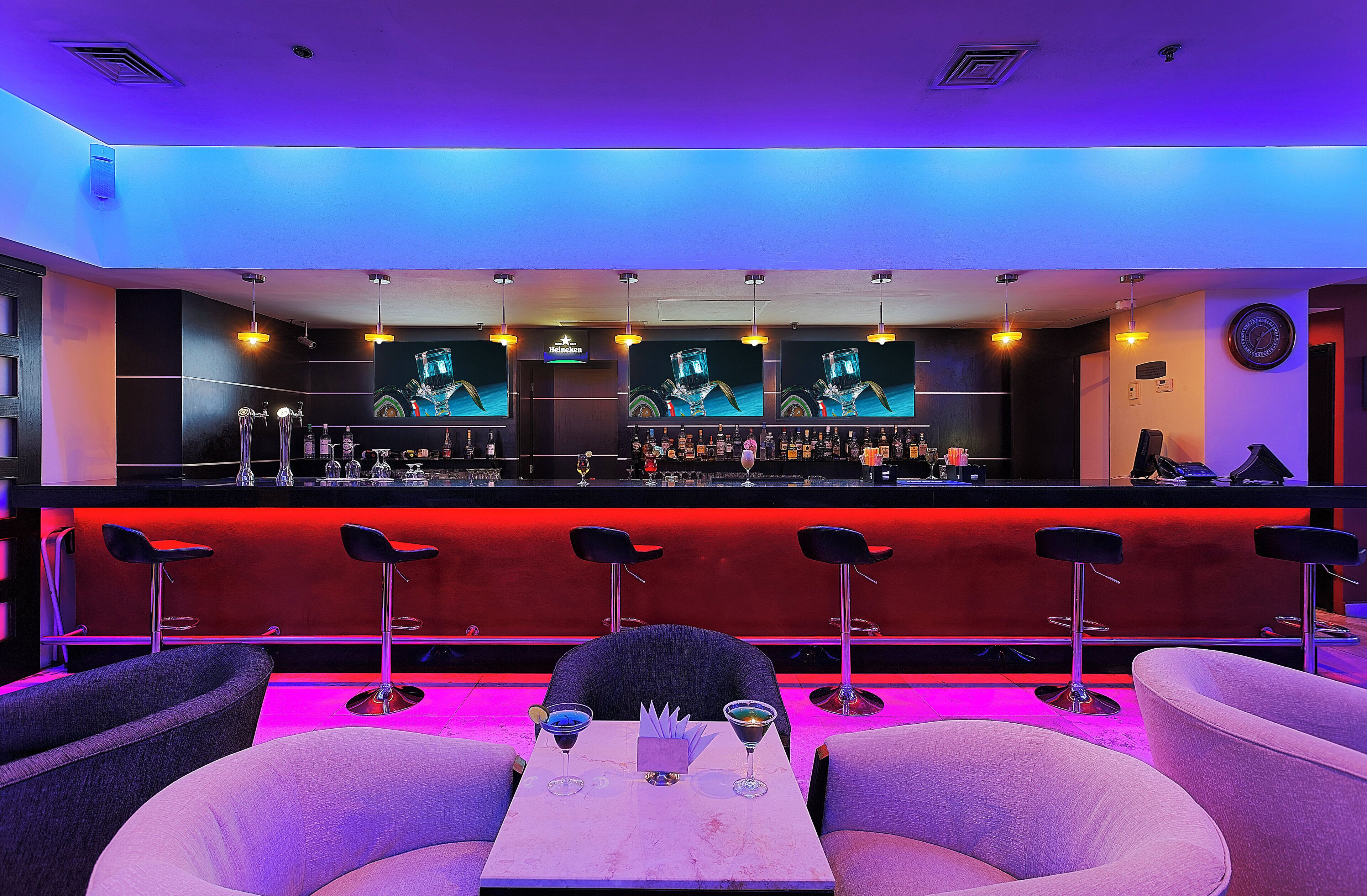 Zona de bar con mostrador, varios taburetes y un área de estar con mesa y sillas.