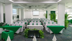 Un salón de conferencias con filas de mesas, sillas y una pantalla para proyector.