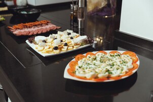 Uma mesa de buffet com diversos alimentos, incluindo queijo, azeitonas e tomates.