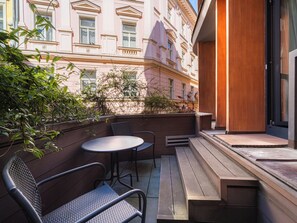 A balcony with a round table and two chairs, a wooden bench, and a view of a pink building with classical architecture. - EA Embassy Prague Hotel (Prague)