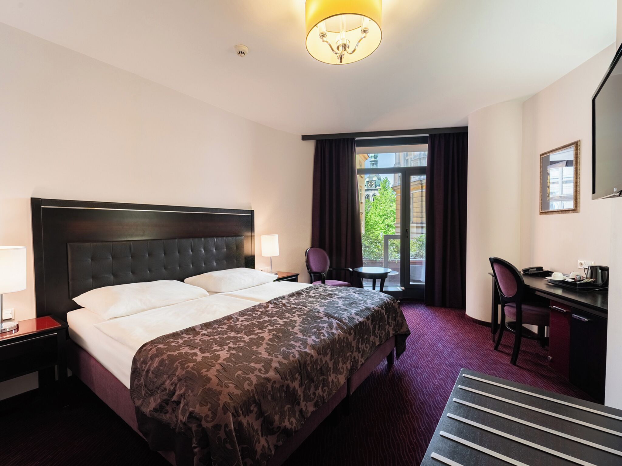 Een hotelkamer met een bed, een bureau, een stoel, een lamp en uitzicht.