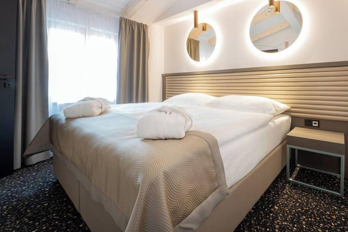 A hotel room with a large bed, two bedside mirrors, a nightstand, and a window with curtains.