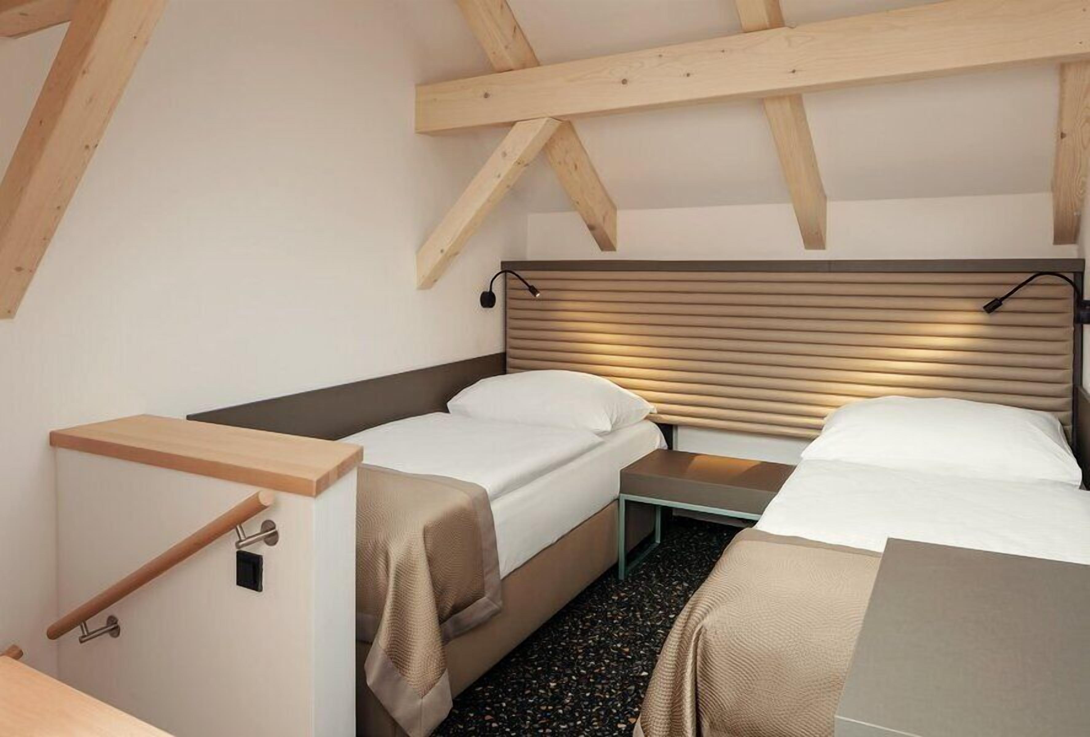 A compact room with two beds, a wooden ceiling, and a small table.