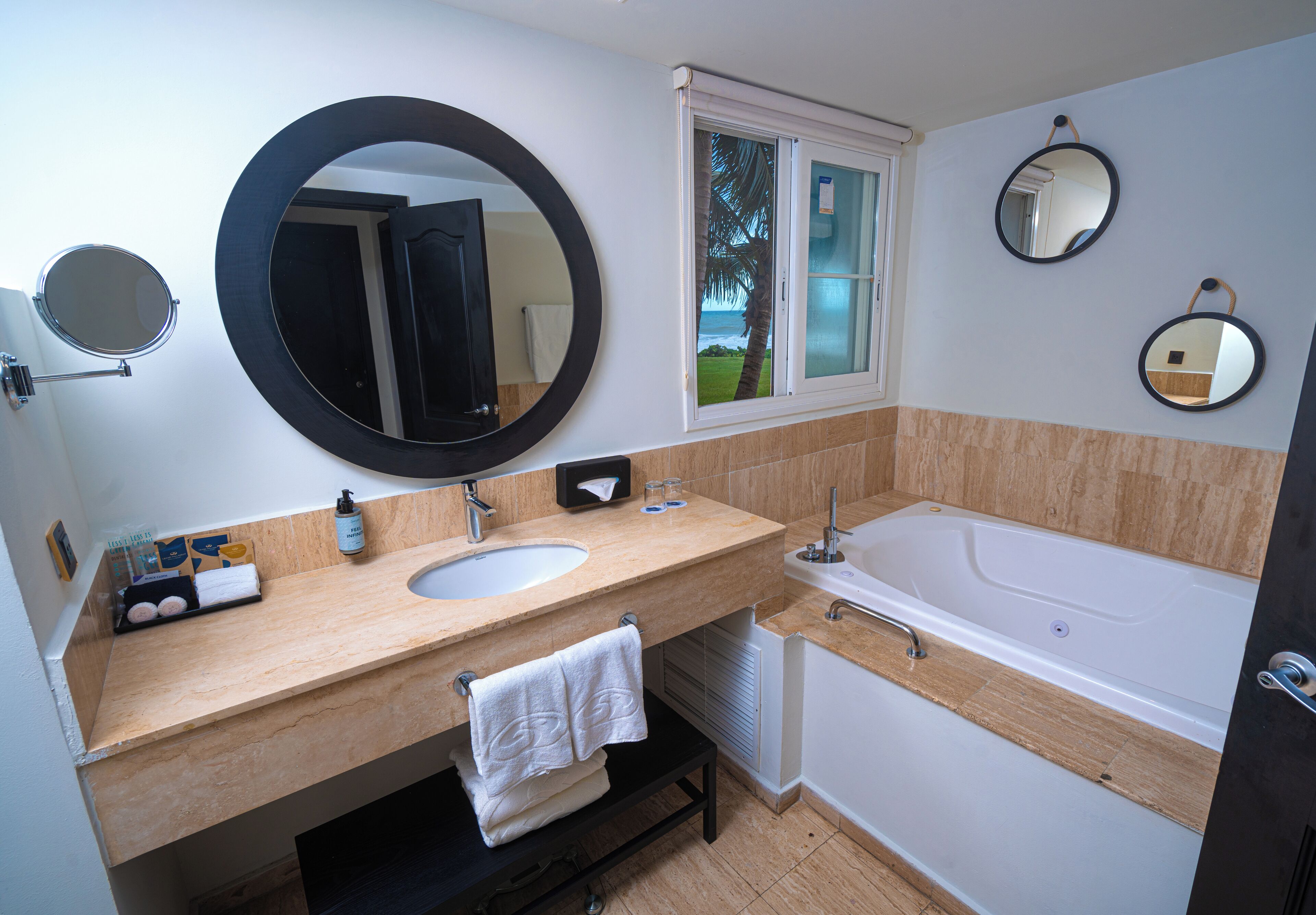 A bathroom with a double sink, a large mirror, a window with a view, and a bathtub.
