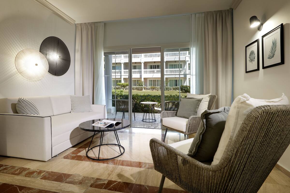 A modern living room with a sofa, armchairs, a coffee table, and a view of a building through large glass doors.
