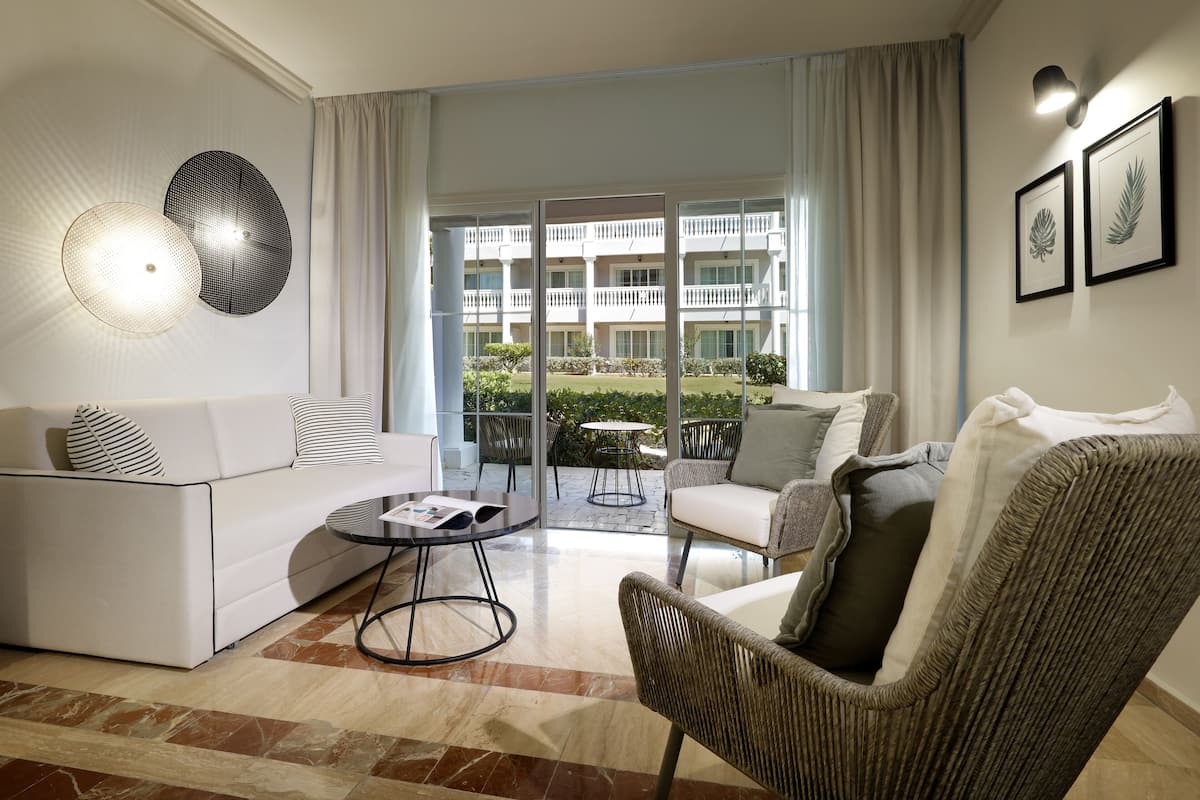 A modern living room with a sofa, armchairs, a coffee table, and a view of a building through large glass doors.