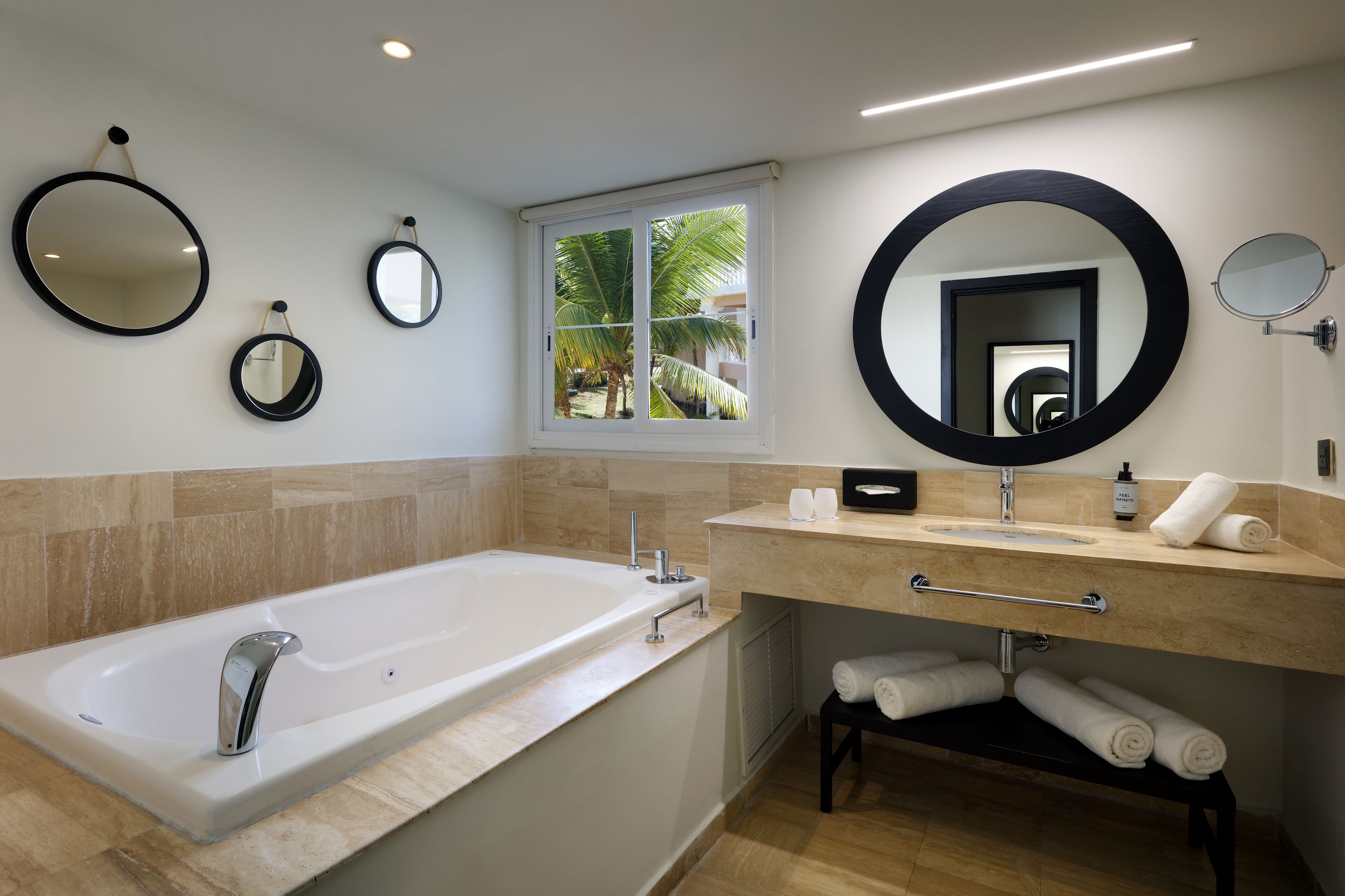 A modern bathroom with a large bathtub, a vanity with a mirror, and towels neatly arranged on a shelf.