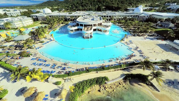 Un complex turístic amb una piscina central, diverses zones de relaxació i una platja.