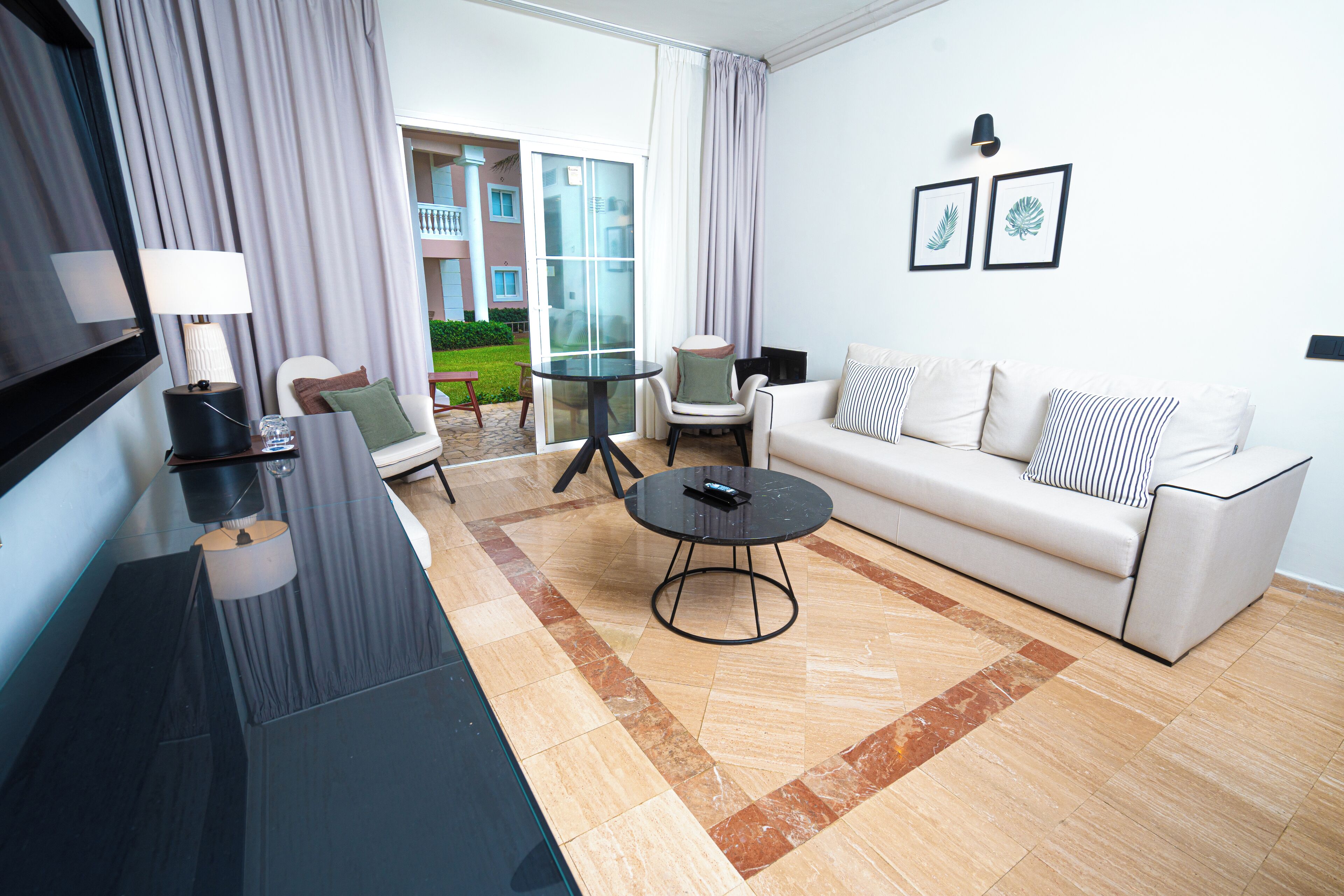 A modern living room with a sofa, a coffee table, and a TV. There is a balcony visible through the glass doors.
