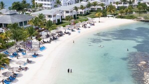 A beach resort with a white sandy beach, clear turquoise water, and a row of white buildings with balconies overlooking the beach.