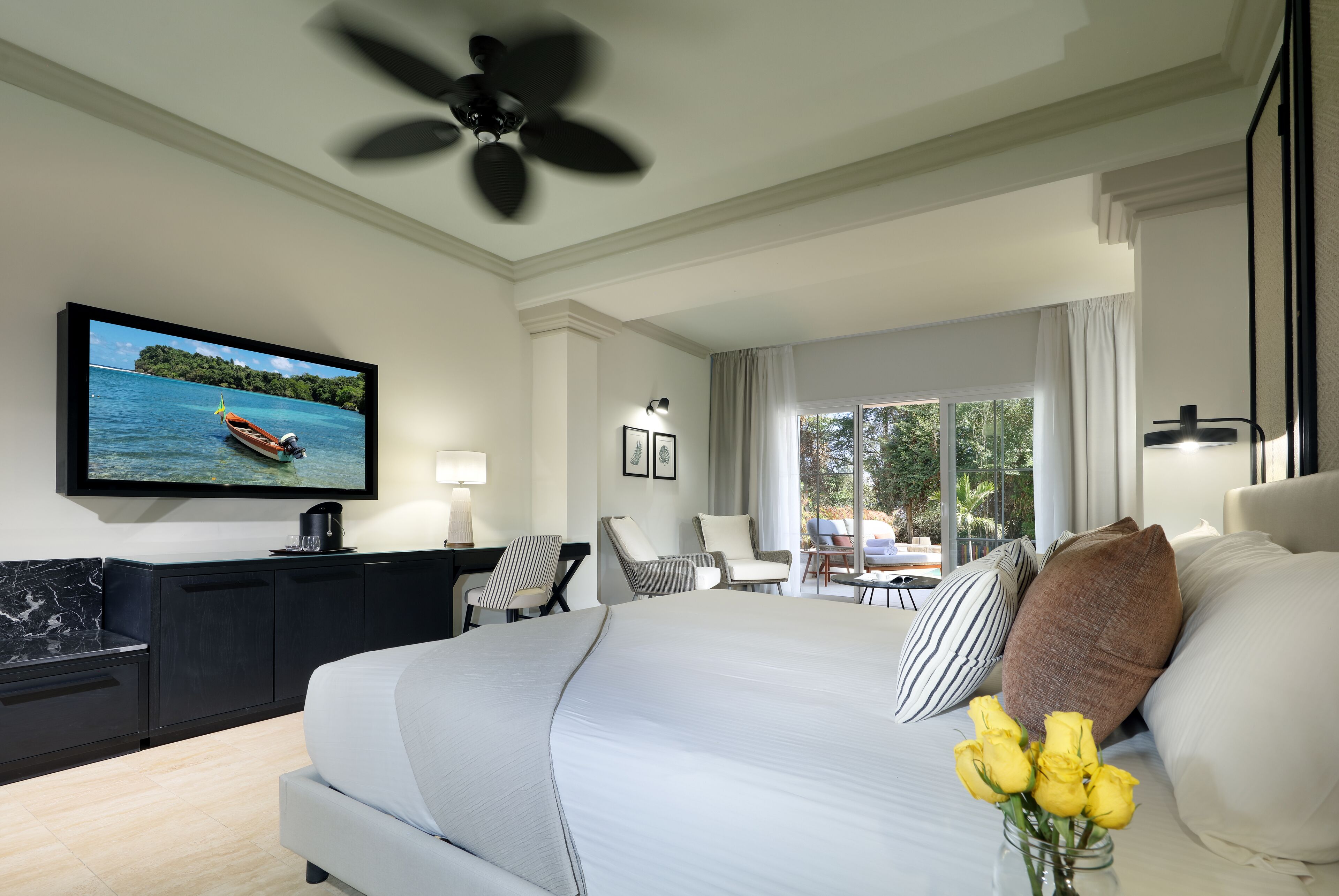 A modern hotel room with a large bed, a TV on the wall, a desk with a chair, and a view of the outdoors.