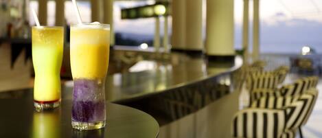 Two drinks on a bar counter with a view of the sky through large windows.