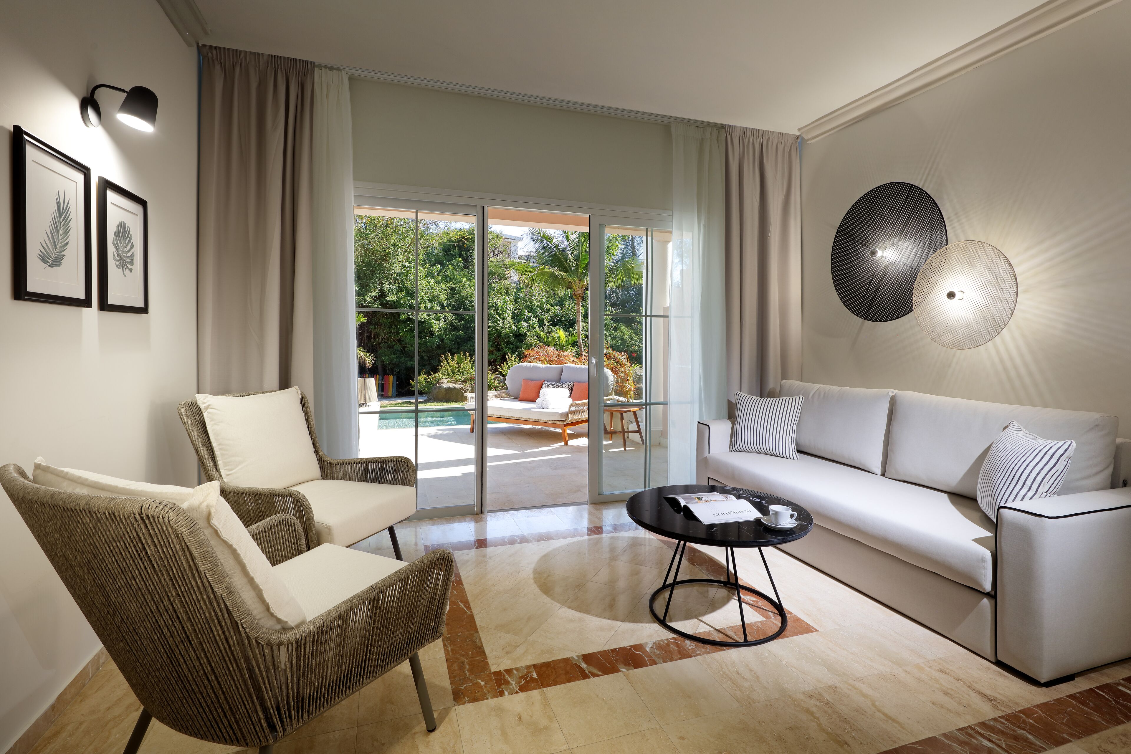 A modern living room with a sofa, two armchairs, a coffee table, and a large glass door leading to an outdoor area with a pool.