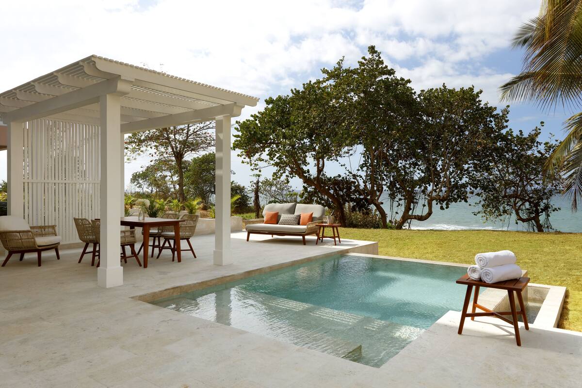 A pool area with a pergola, outdoor furniture, and a view of the ocean.