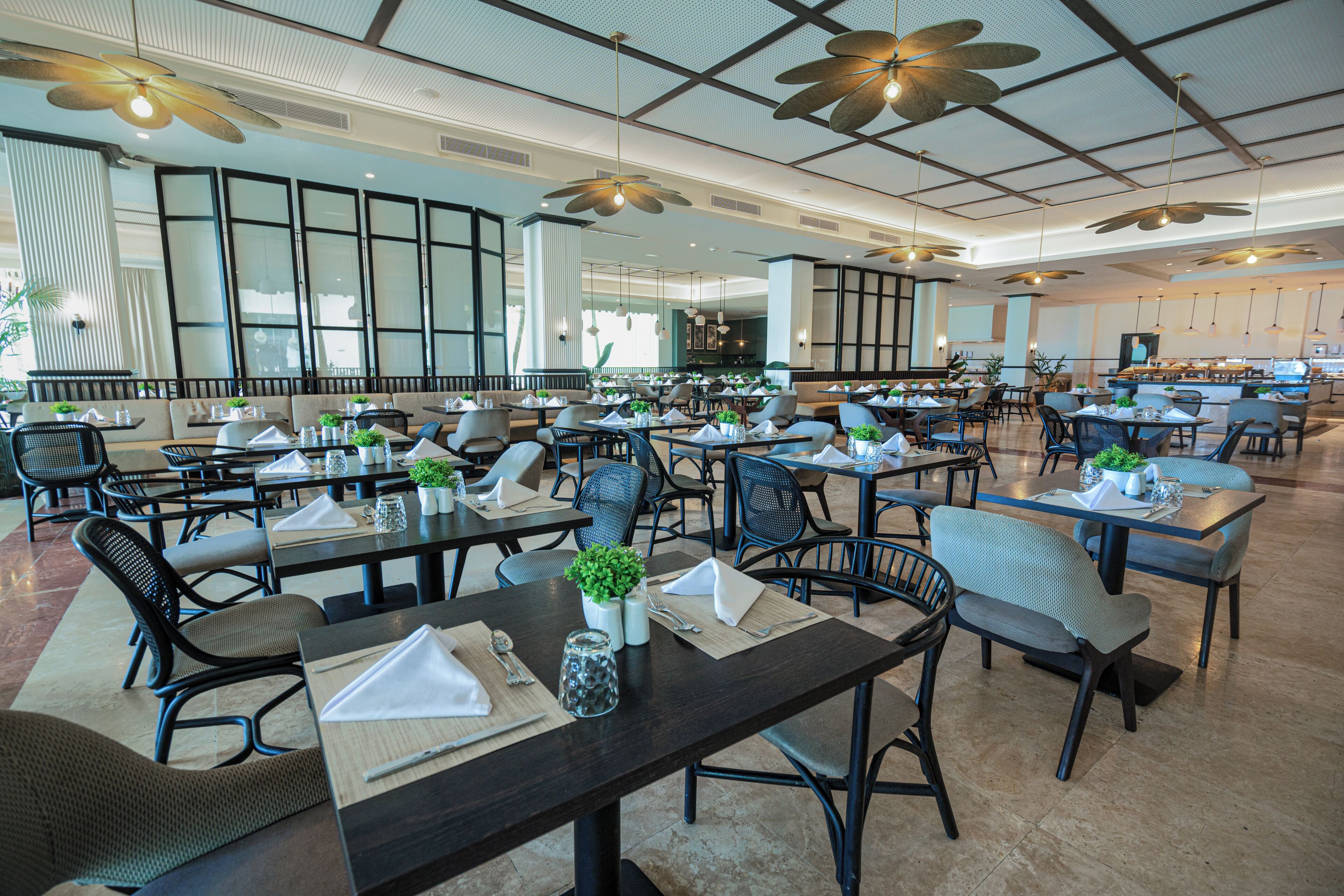 A spacious dining area with multiple tables and chairs, large windows, and ceiling fans.