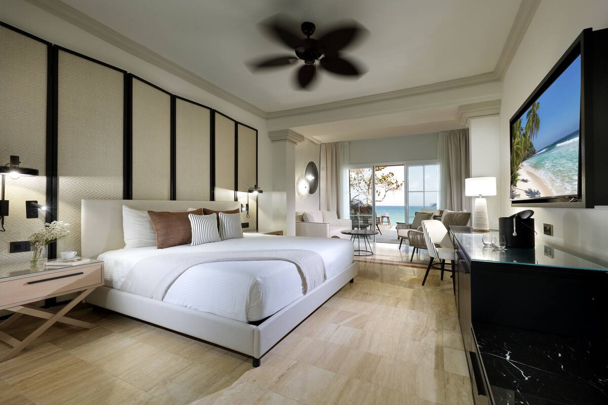 A modern hotel room with a large bed, a desk with a computer, a TV, and a view of the ocean.