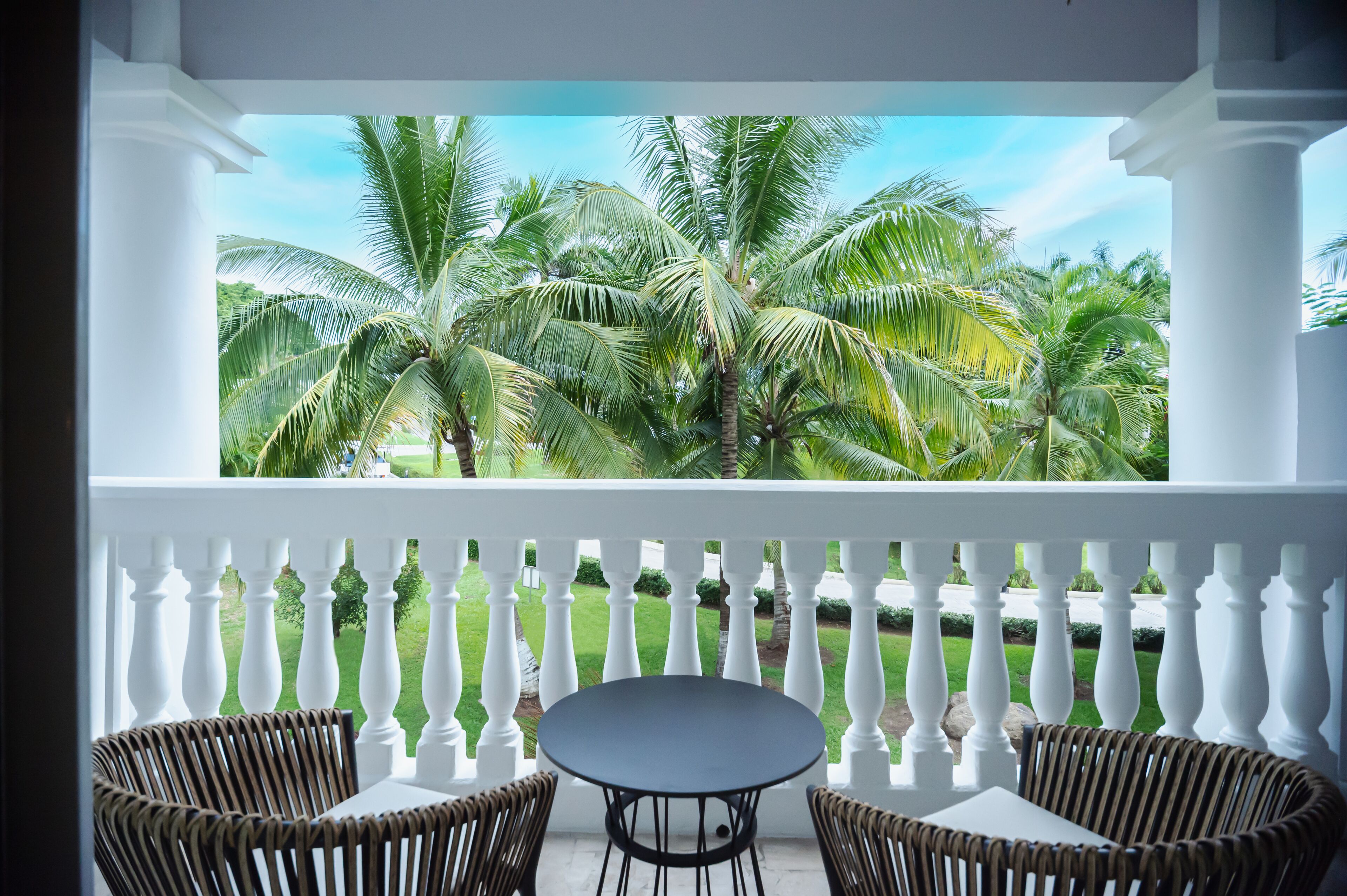 A balcony with white balustrades, two wicker chairs, and a round table.