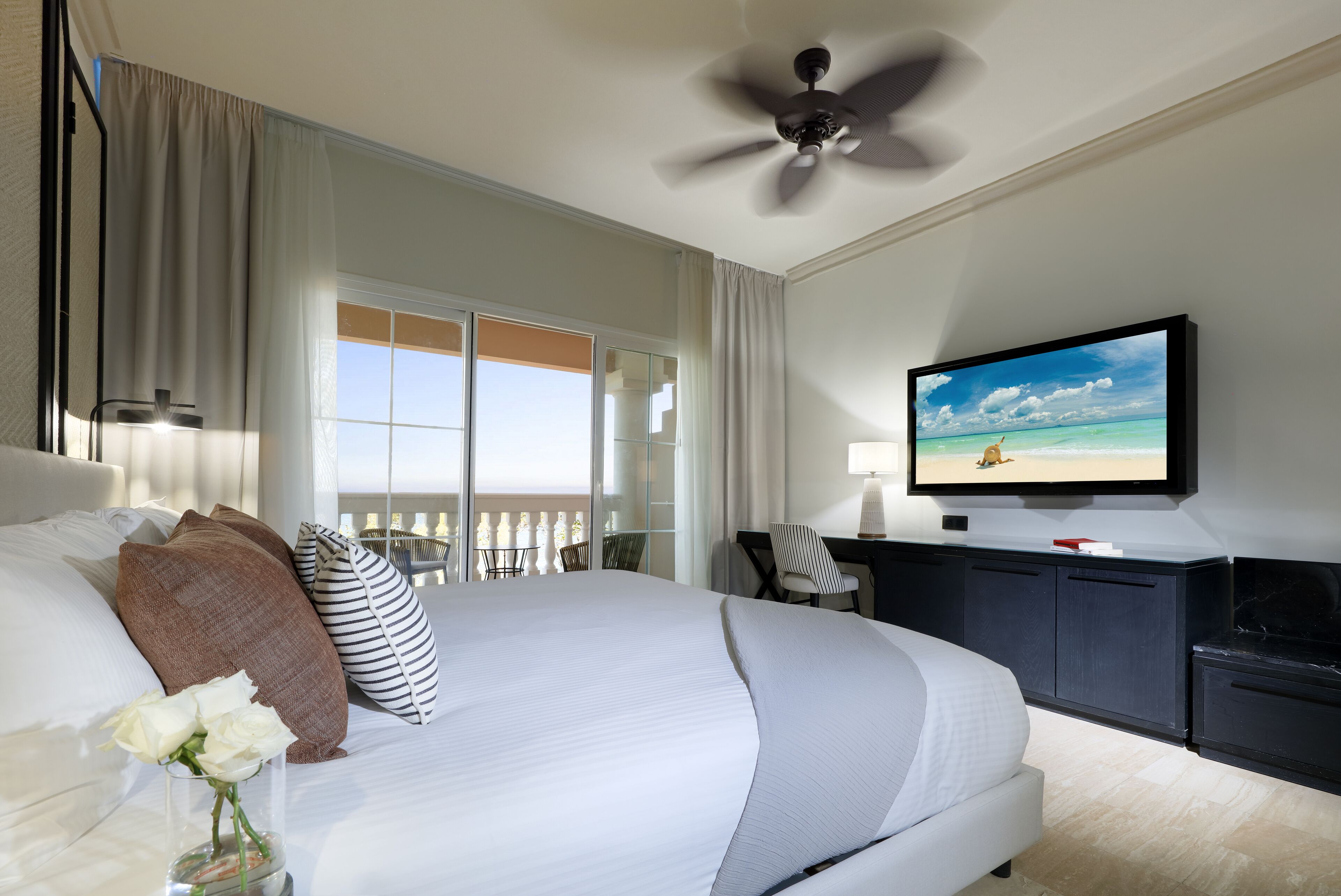 A hotel room with a large bed, a television, a desk, and a view of the ocean.
