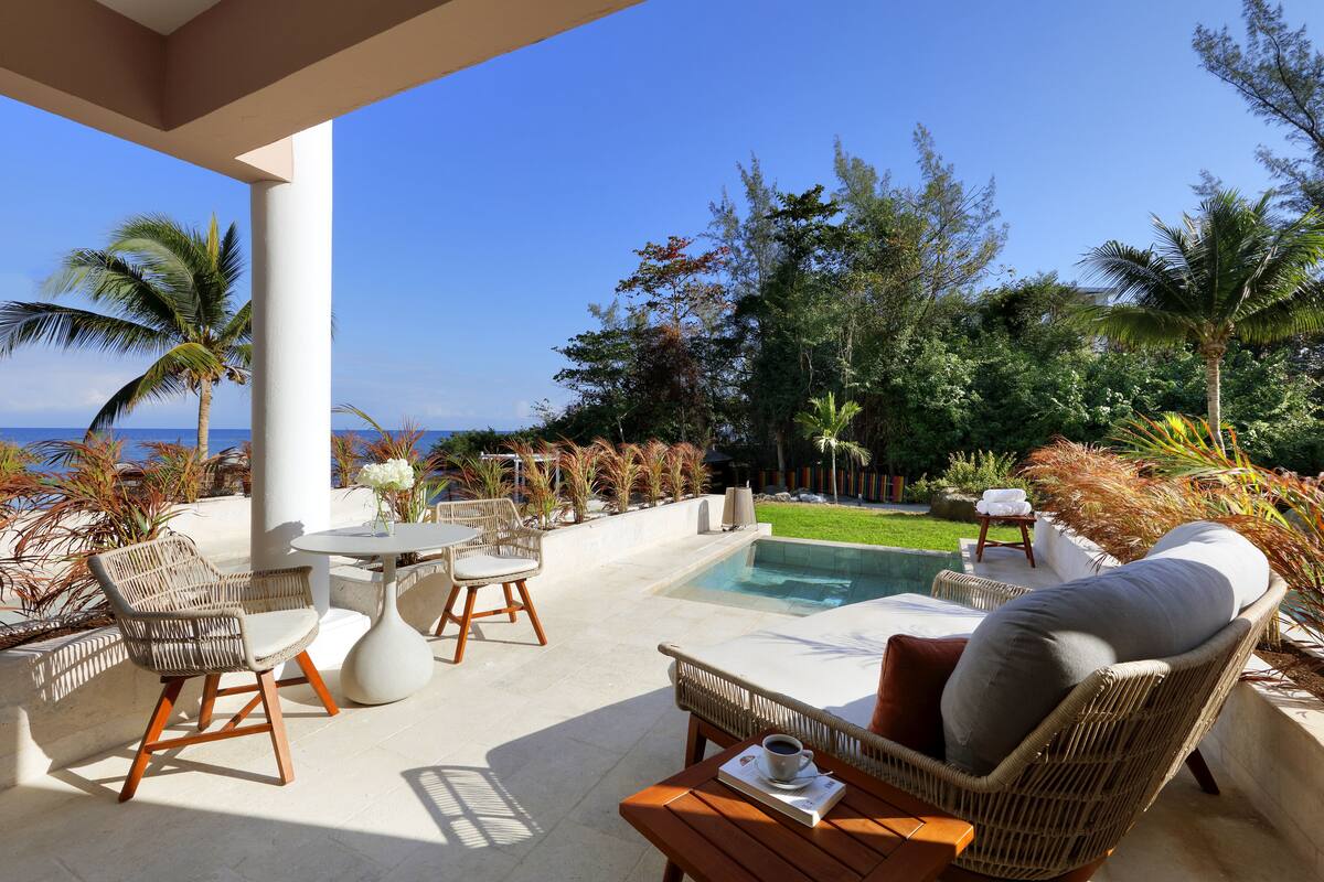 A poolside area with wicker furniture, a table with a drink, and a view of the ocean.