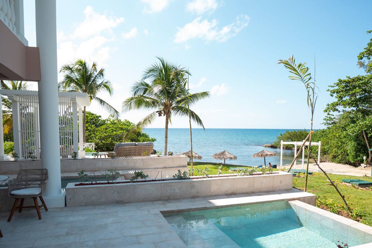 A pool area with a view of the ocean, palm trees, and a covered seating area.