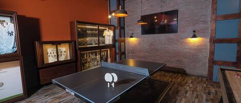 Una mesa de ping pong en una habitación con pared de ladrillo, cuadros enmarcados e iluminación colgante.
