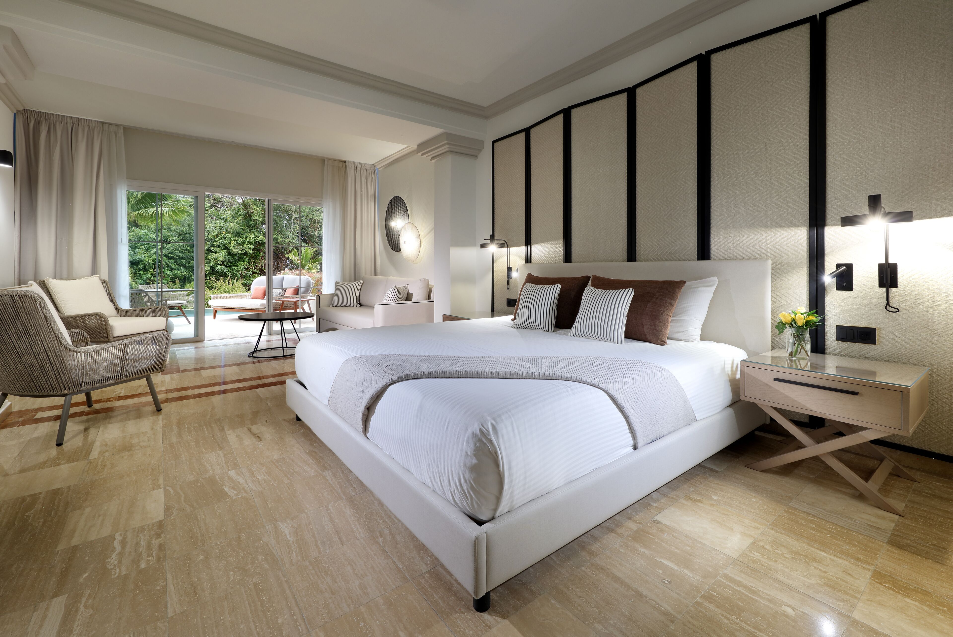 A modern hotel room with a large bed, a sitting area with a chair and a table, and a view of the outdoors.