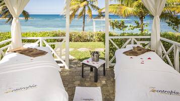 Relax under a serene canopy with two plush beds, a small table, and a tranquil ocean view.