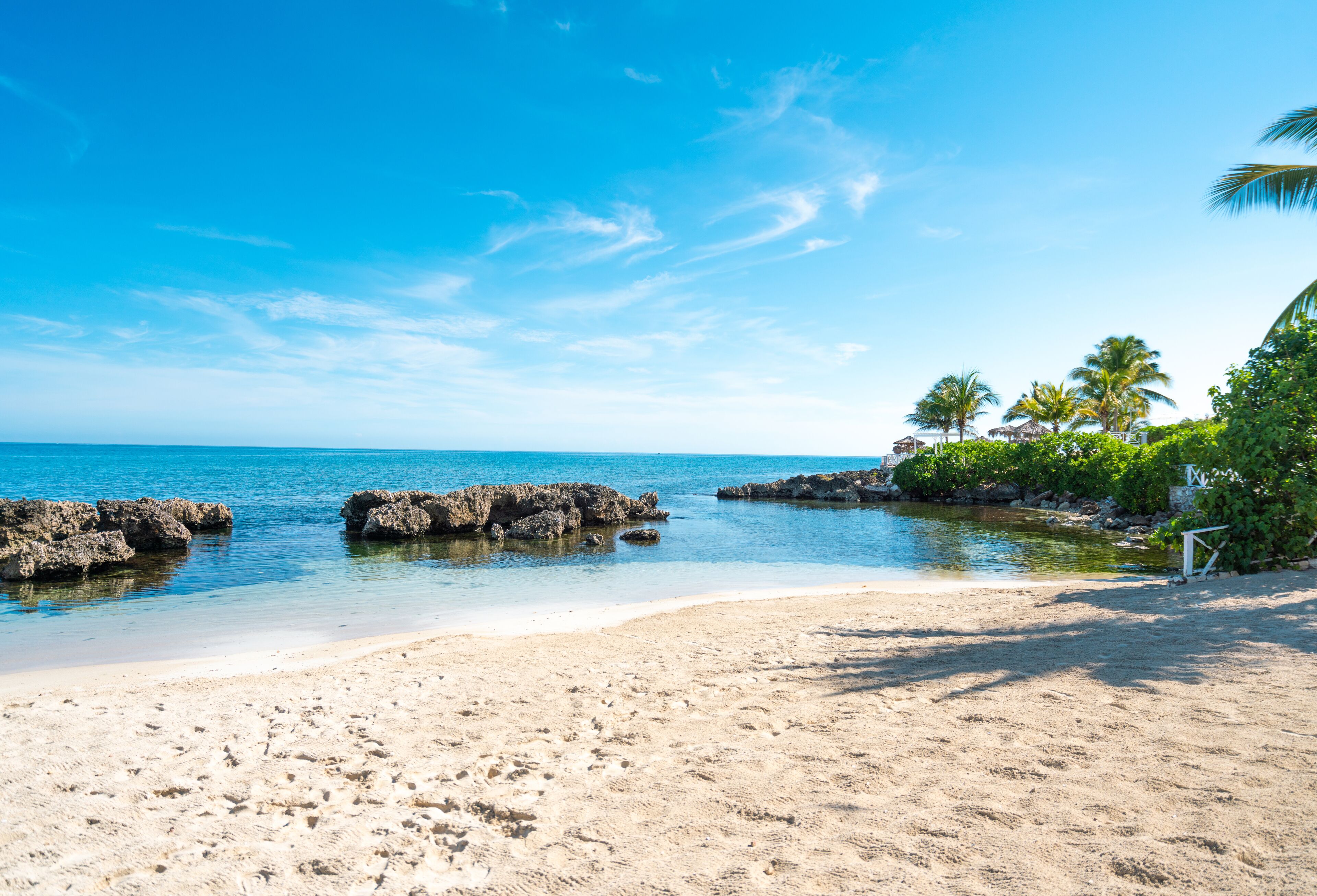 A beach with clear blue water, rocky outcrops, and palm trees.