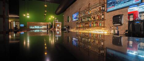 A bar area with a brick wall, shelves of bottles, a television screen, and a polished floor.