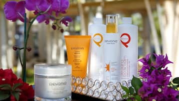 A display of Pevonia skincare products including a jar, a tube, and two bottles, surrounded by flowers.