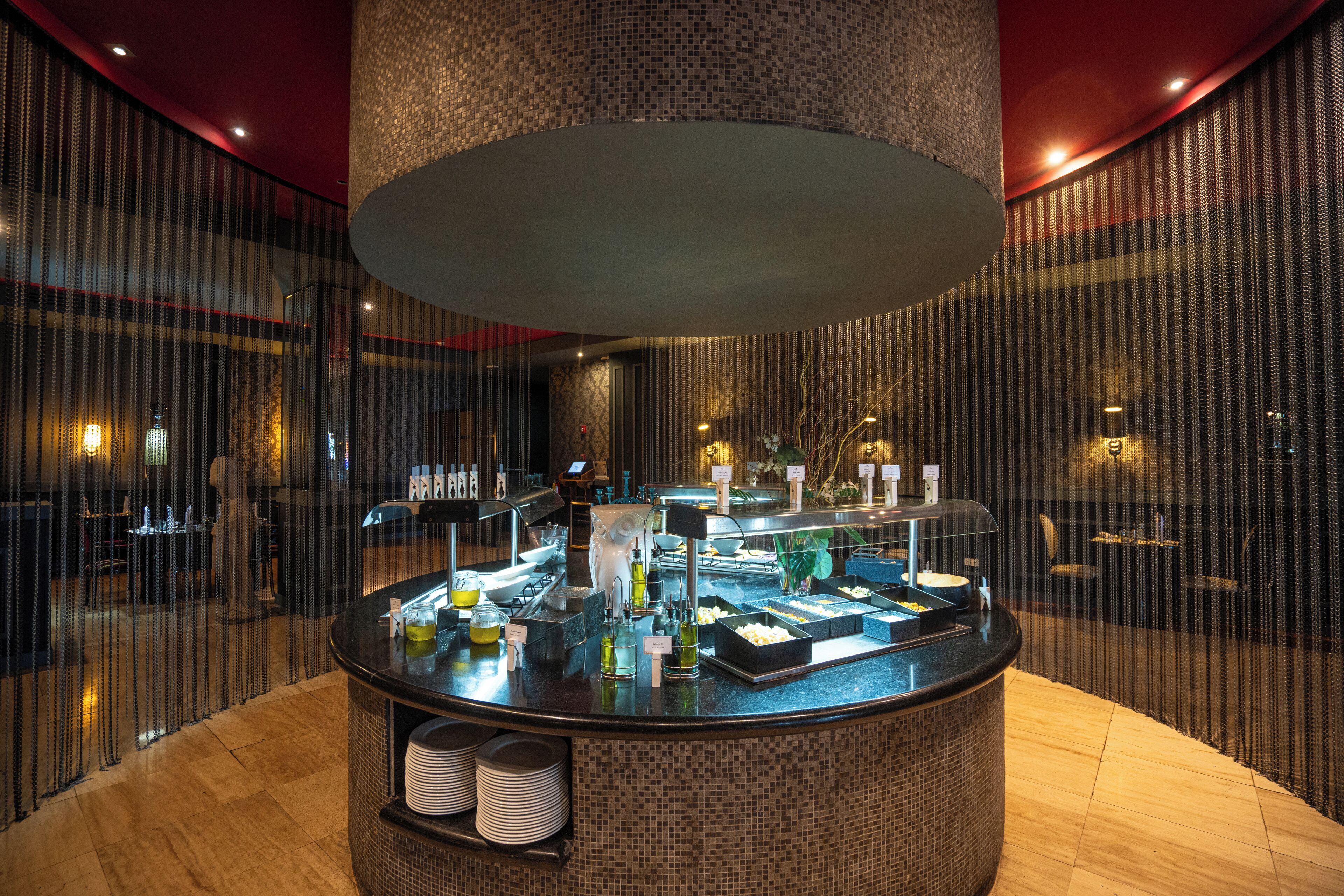 Ein Frühstücksbuffet mit verschiedenen Speisen und Beilagen, umgeben von einer gemusterten Wand und einer großen, strukturierten Decke.