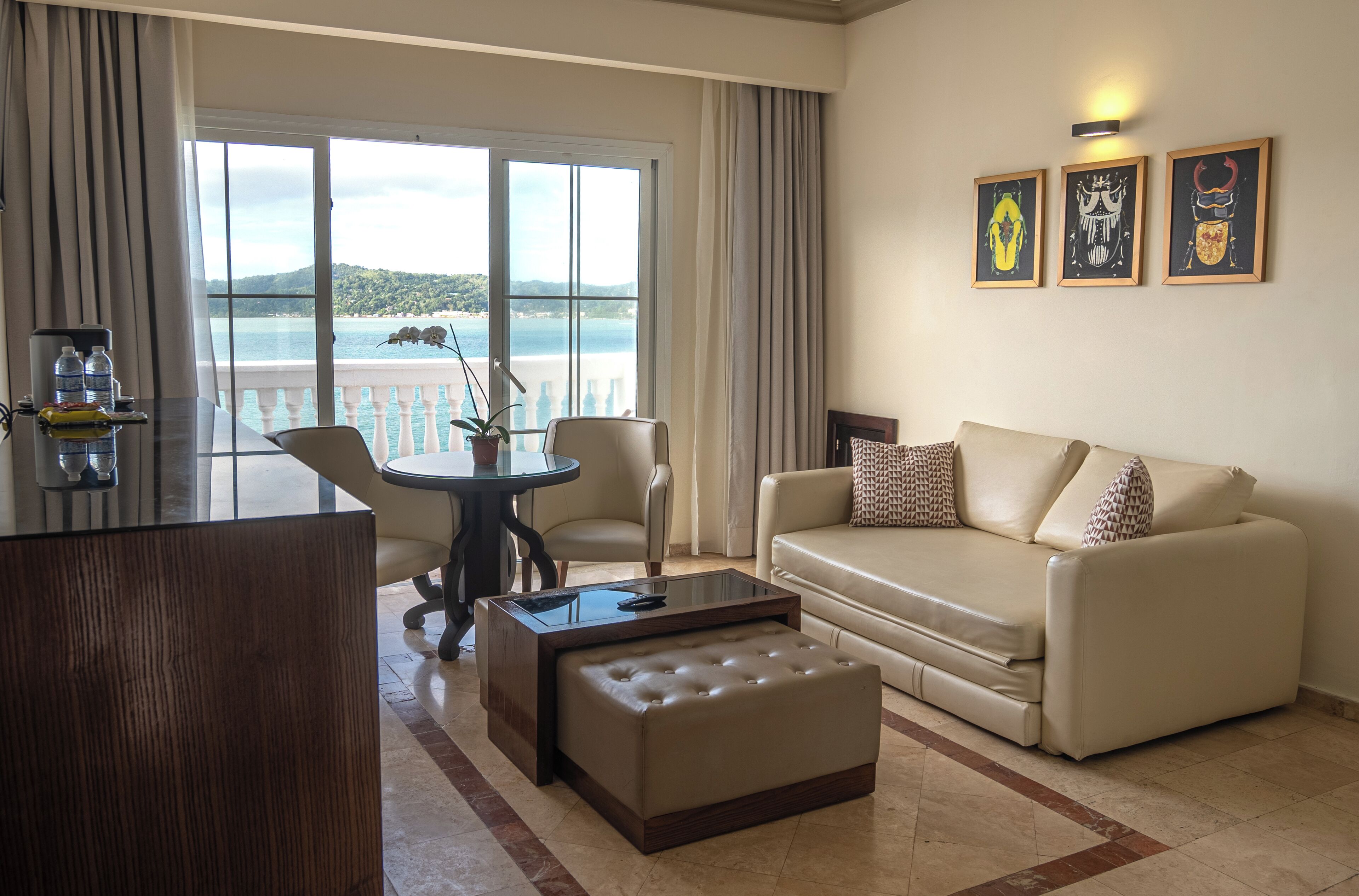 A hotel room with a balcony, a sofa, a coffee table, and a dining table.