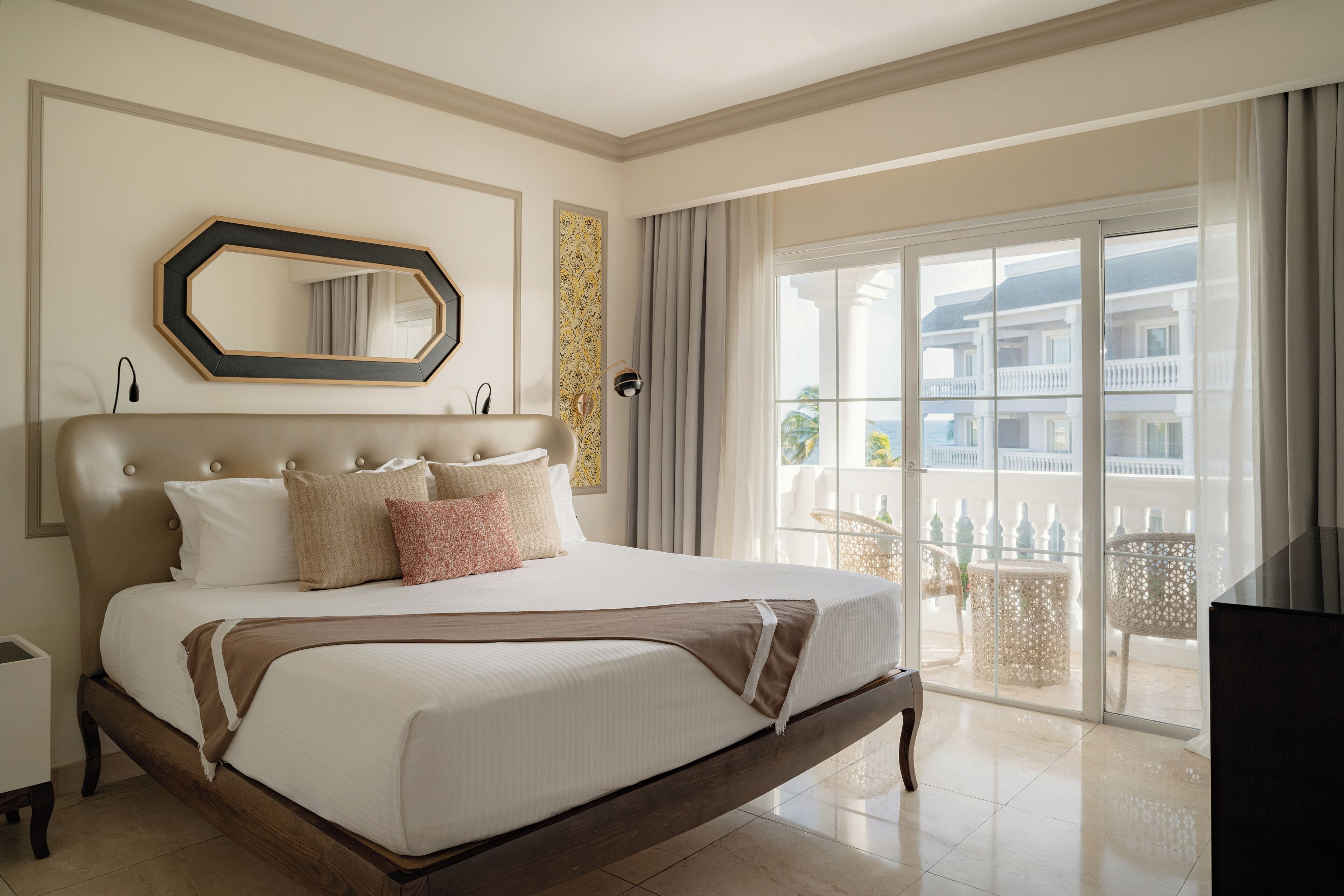 A hotel room with a large bed, a mirror, a window with a view of buildings, and a balcony.