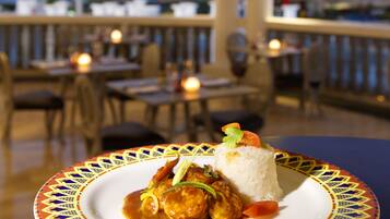 A table with a plate of food, a view of the ocean, and a railing with lights.
