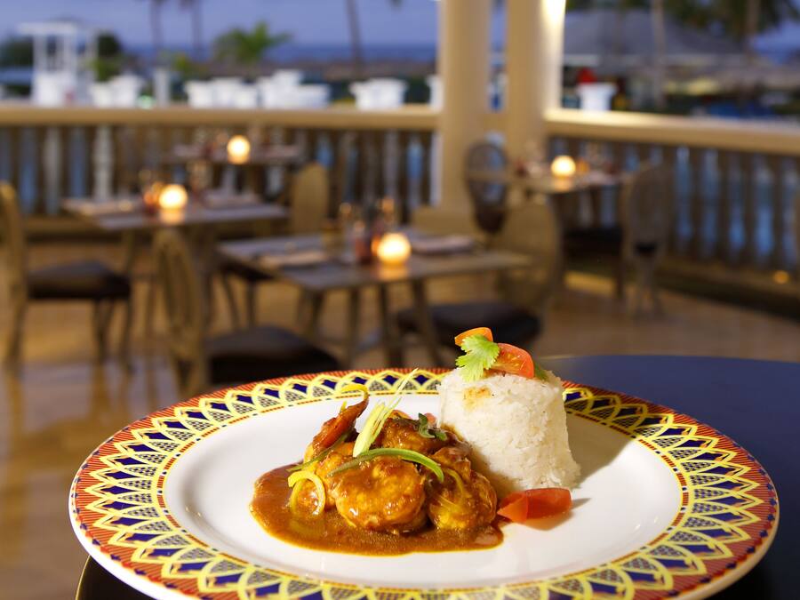 A table with a plate of food, a view of the ocean, and a railing with lights.