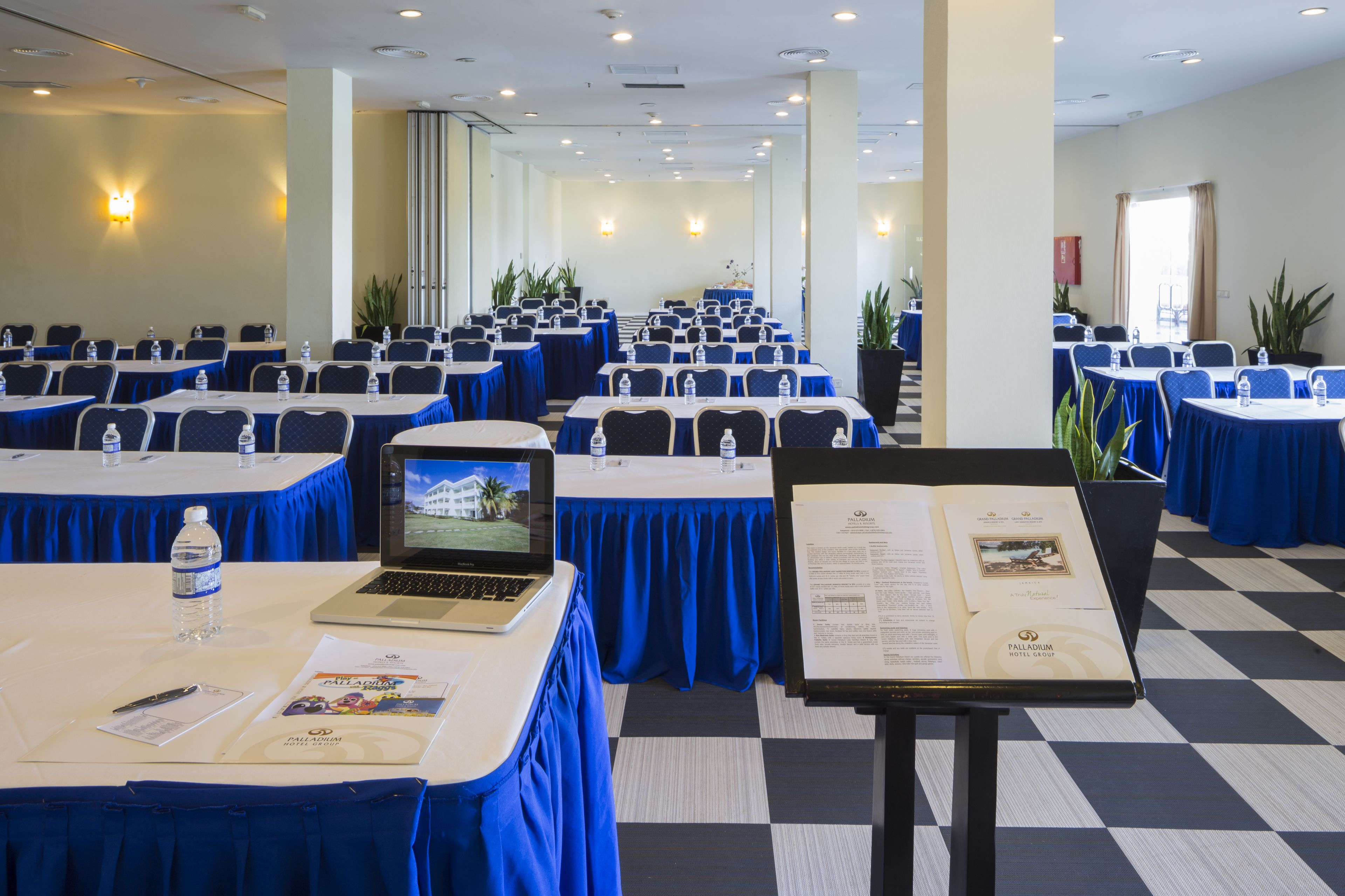 A conference room with tables set up for a meeting, laptops, water bottles, and informational brochures.