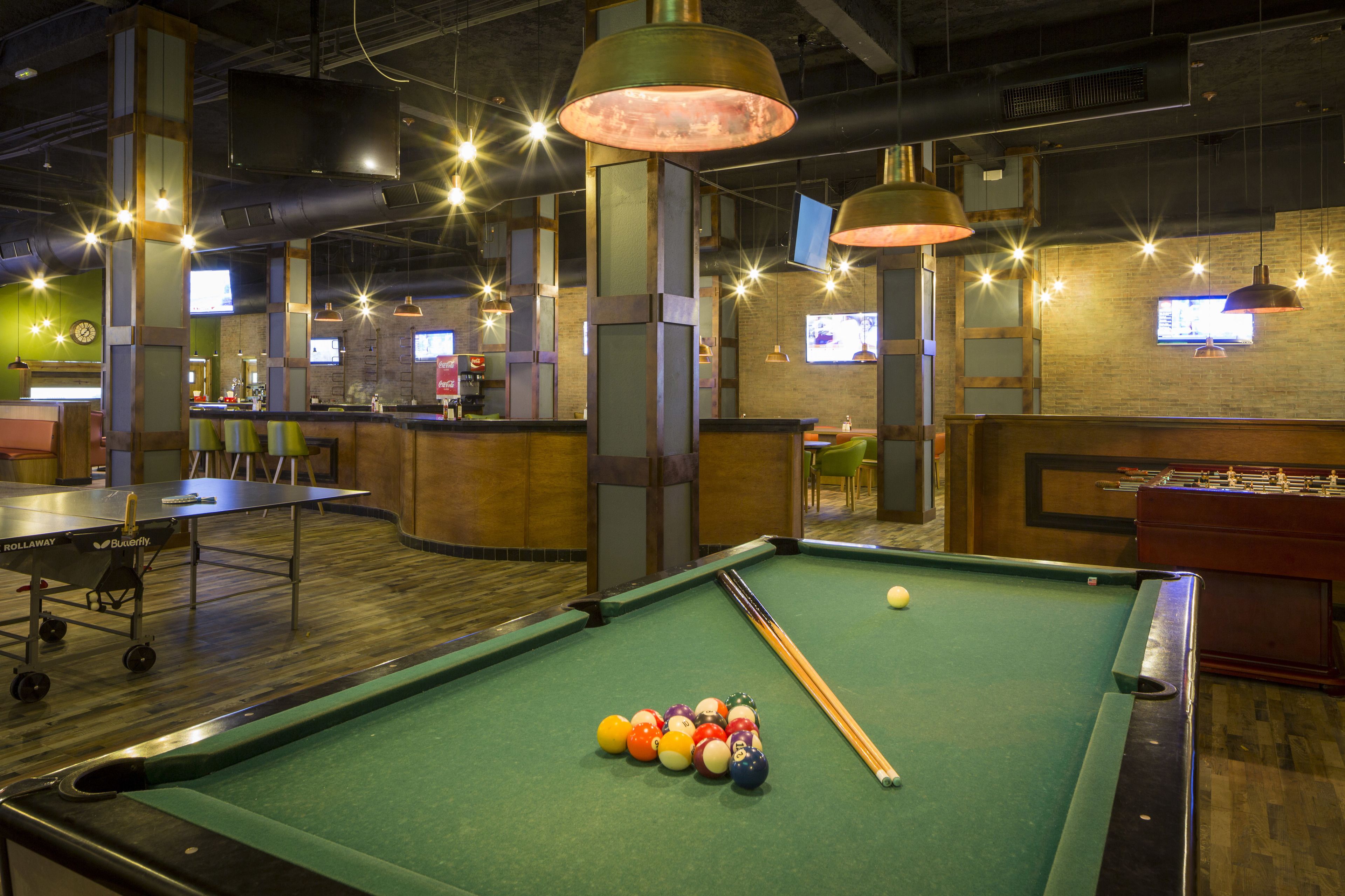 Une table de billard avec des billes, une table de baby-foot et un coin bar avec un comptoir et des chaises.