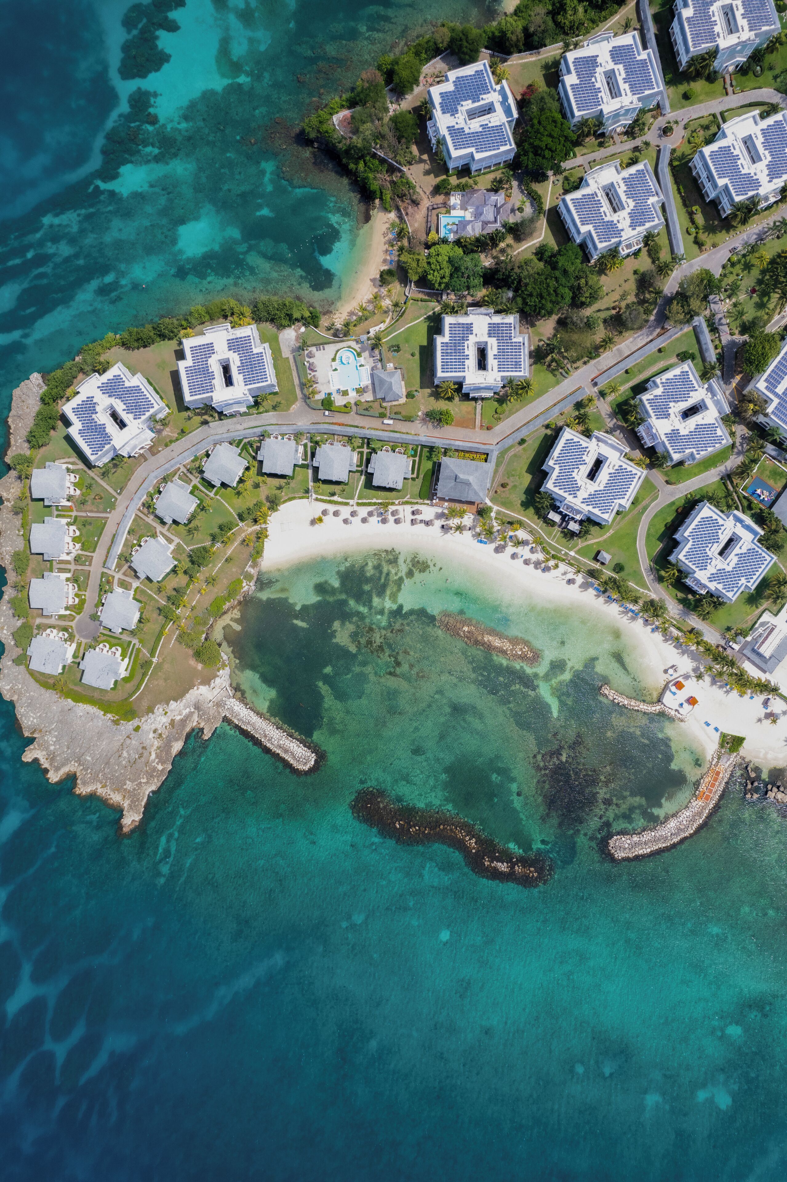 An aerial view of a coastal resort with multiple buildings, a beach, and clear turquoise waters.