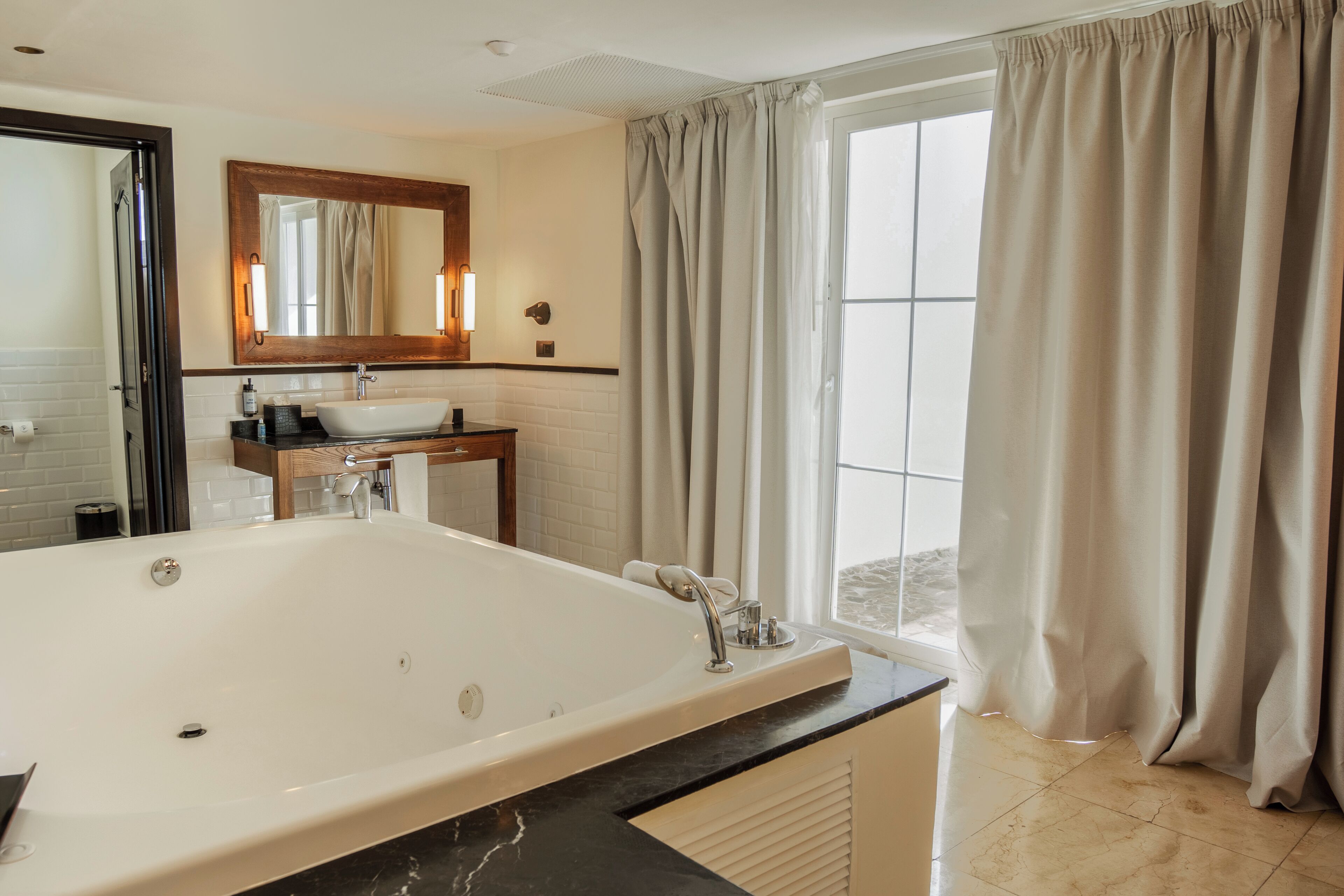 Ein modernes Badezimmer mit einer großen Badewanne, einem Waschtisch inklusive Spiegel und einem Fenster mit Vorhängen.