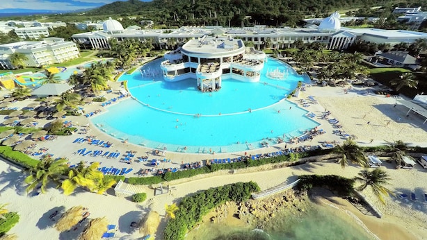 A resort with a central pool, multiple lounge areas, and a beach.
