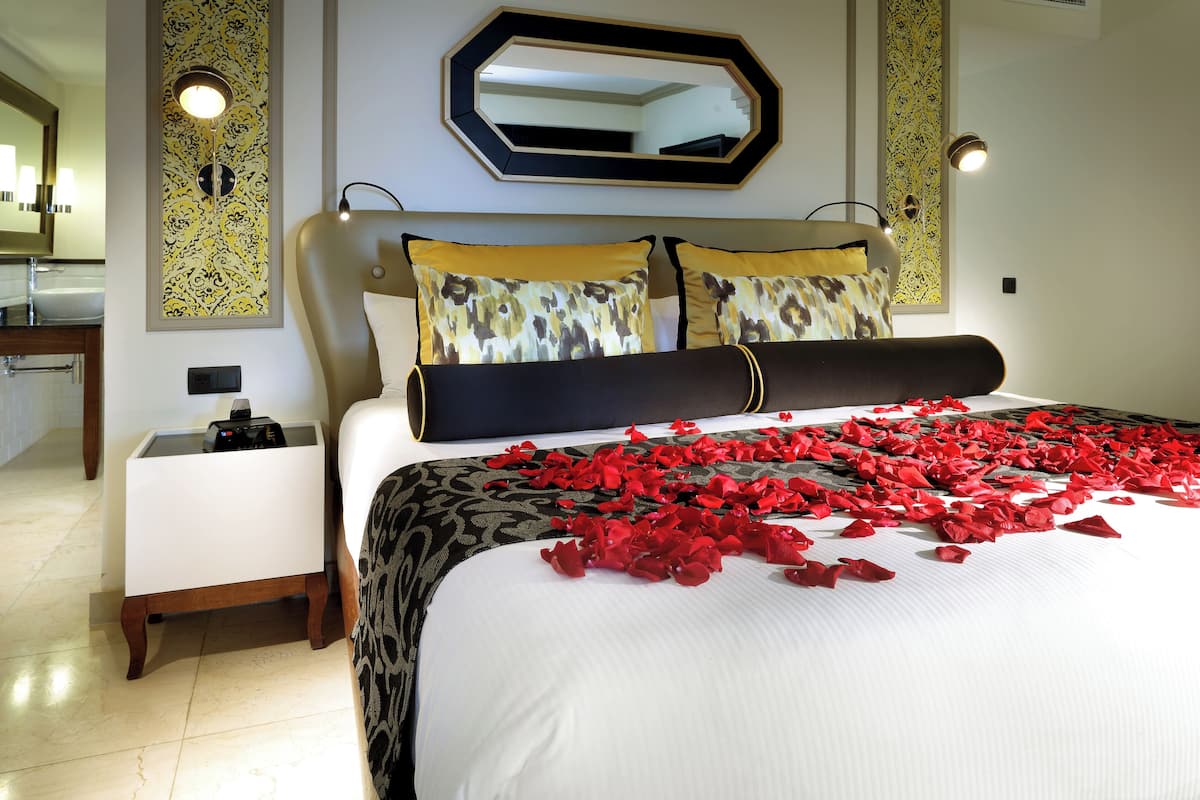A hotel room with a large bed, a bedside table, a mirror, and a wall with decorative panels.