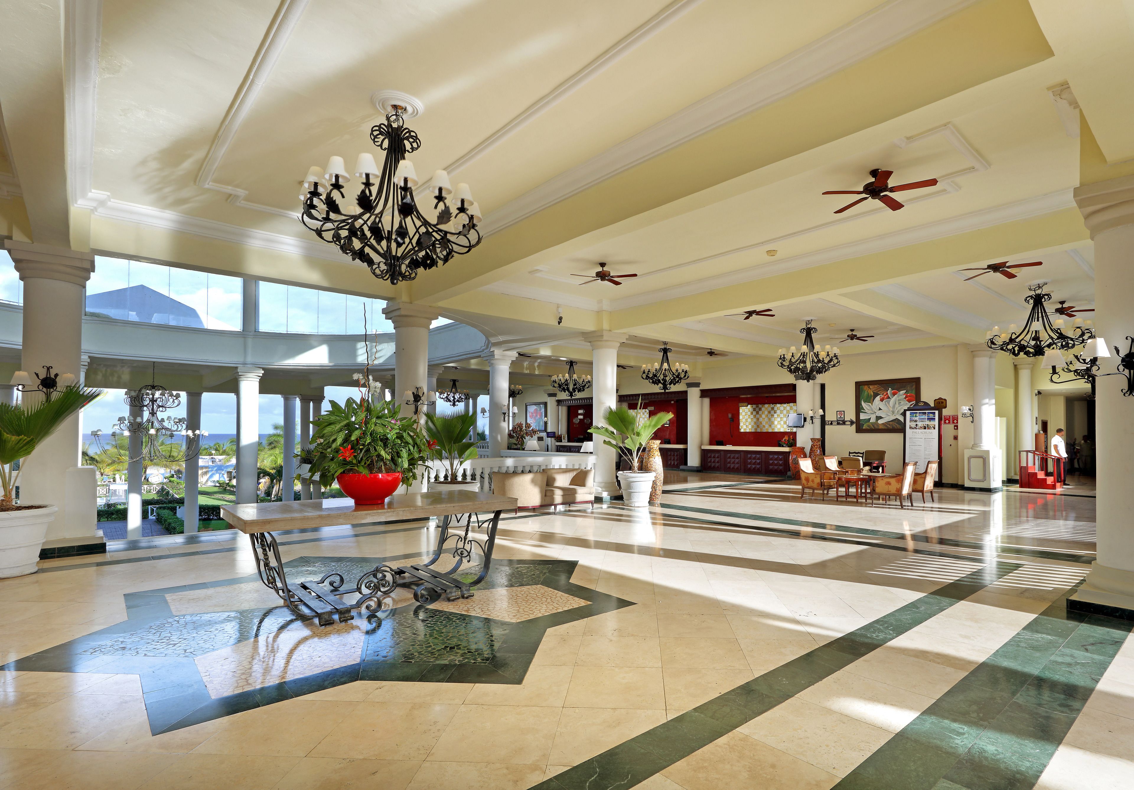 A spacious lobby with high ceilings, chandeliers, and large windows offering a view of the outdoors.