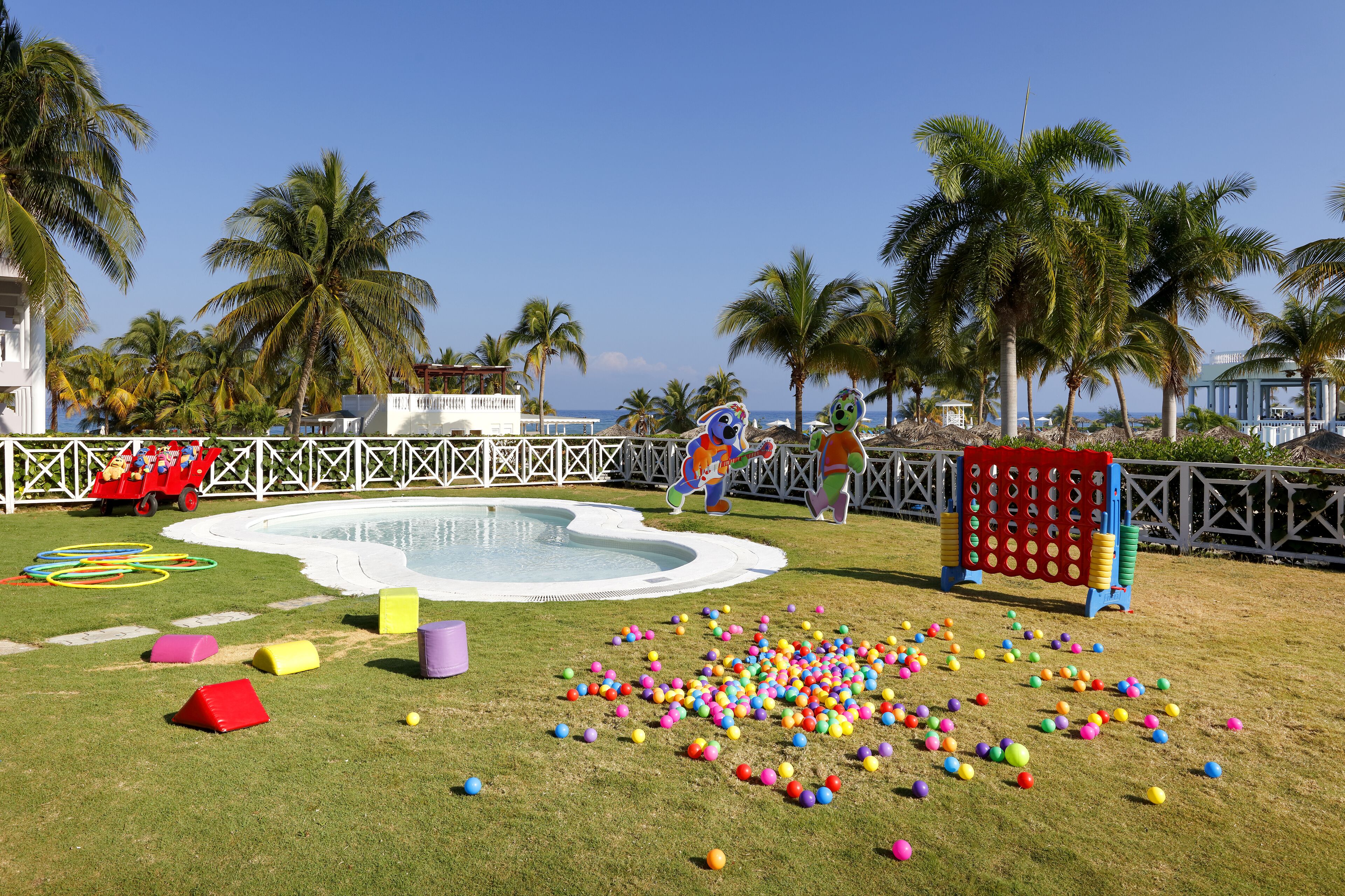 Zona de piscina con piscina infantil, pelotas de colores y estructuras de juego.