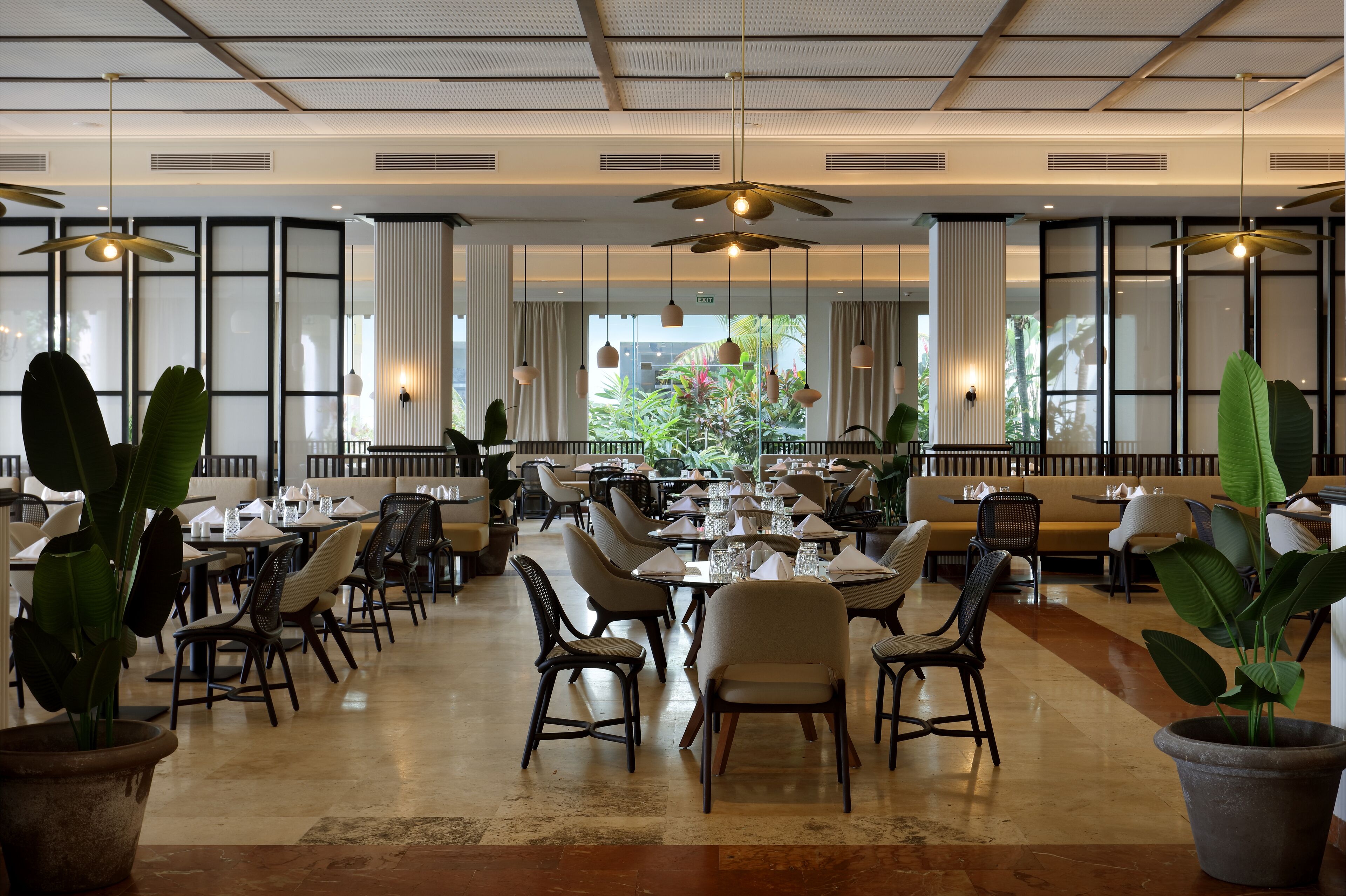 A spacious dining area with multiple tables and chairs, ceiling fans, and large windows with curtains.