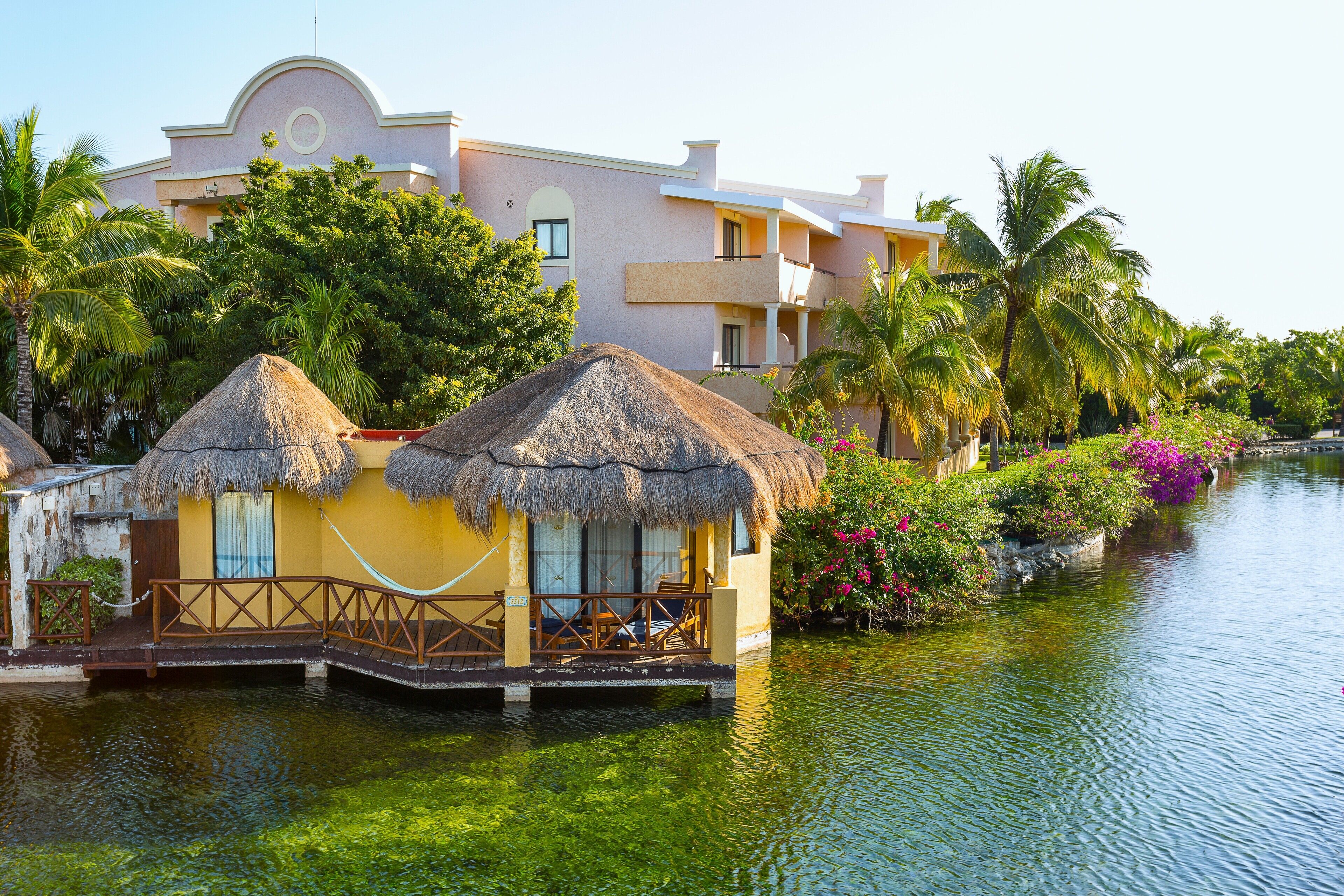 Overwater bungalows with thatched roofs, a pool, and lush greenery.