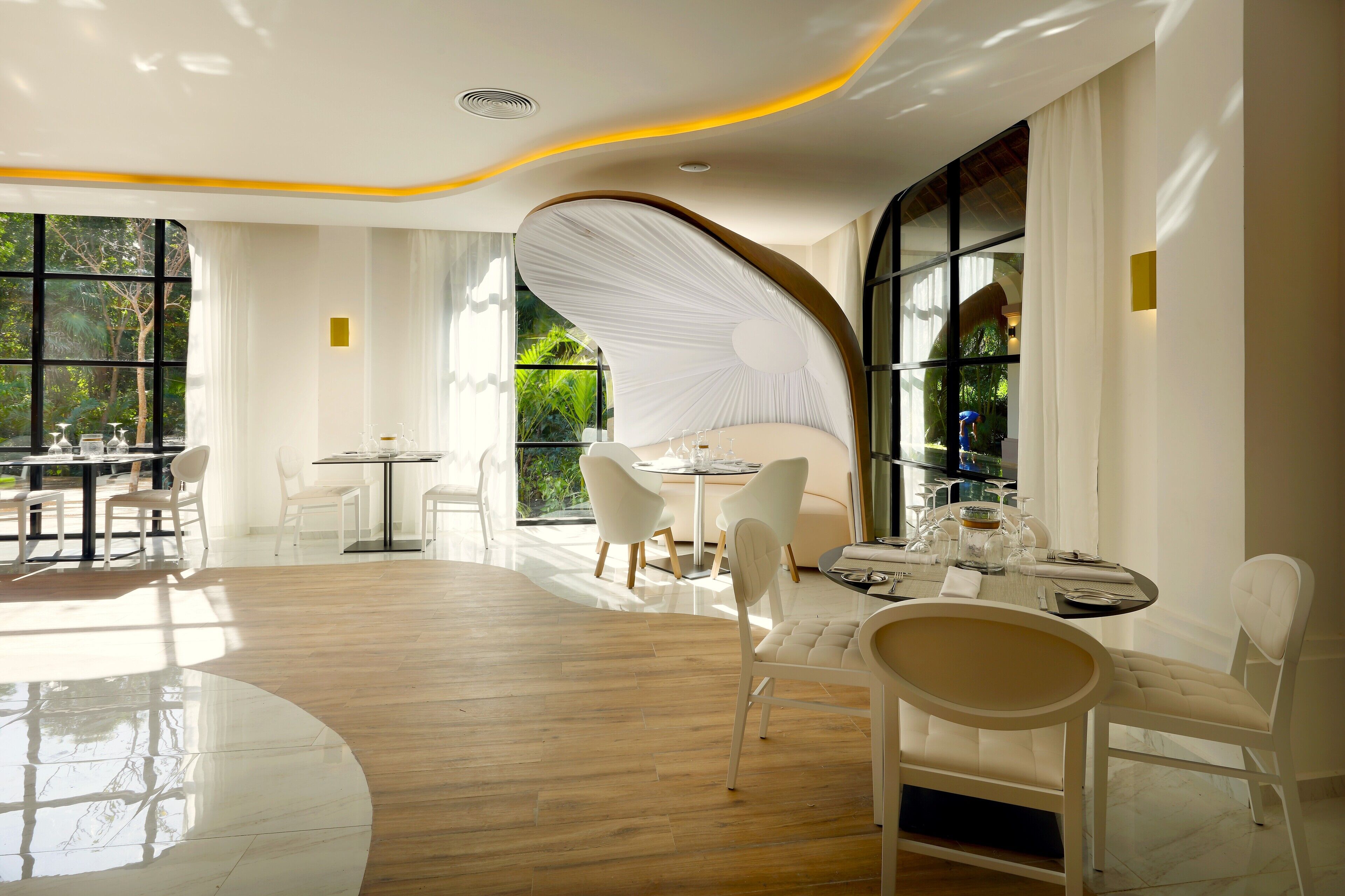 A modern dining area with white furniture, large windows, and a curved ceiling design.
