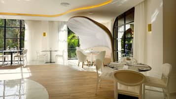 A modern dining area with white furniture, large windows, and a curved ceiling design.