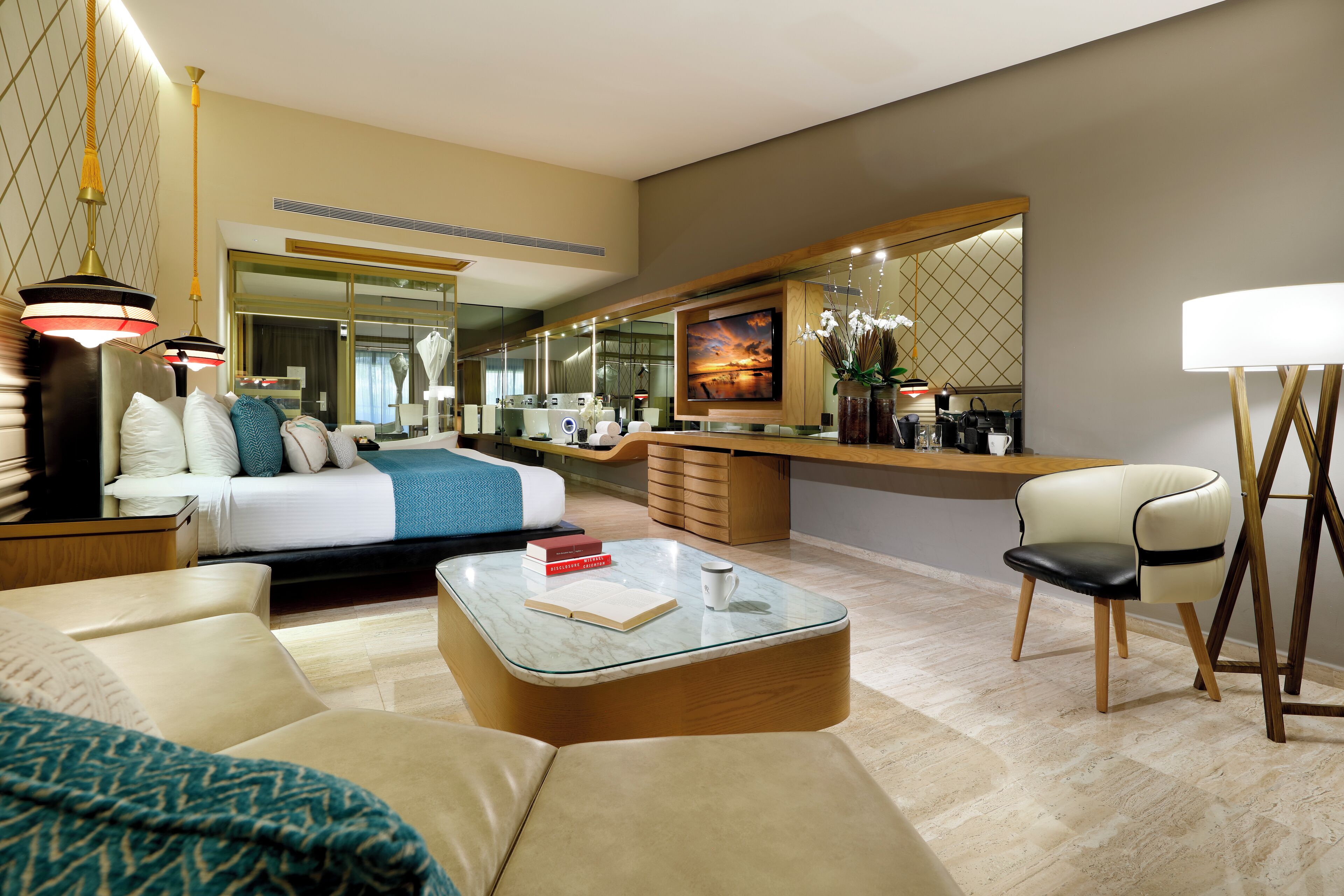 A modern hotel room with a large bed, a sitting area with a coffee table, a desk, and a large mirror.